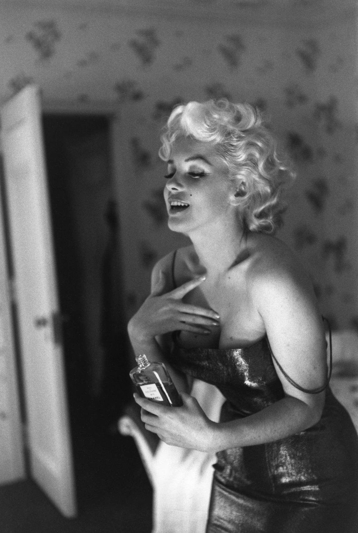 Aktorka Marilyn Monroe ubrana w suknię na ramiączka trzyma w ręku perfumy Chanel No. 5