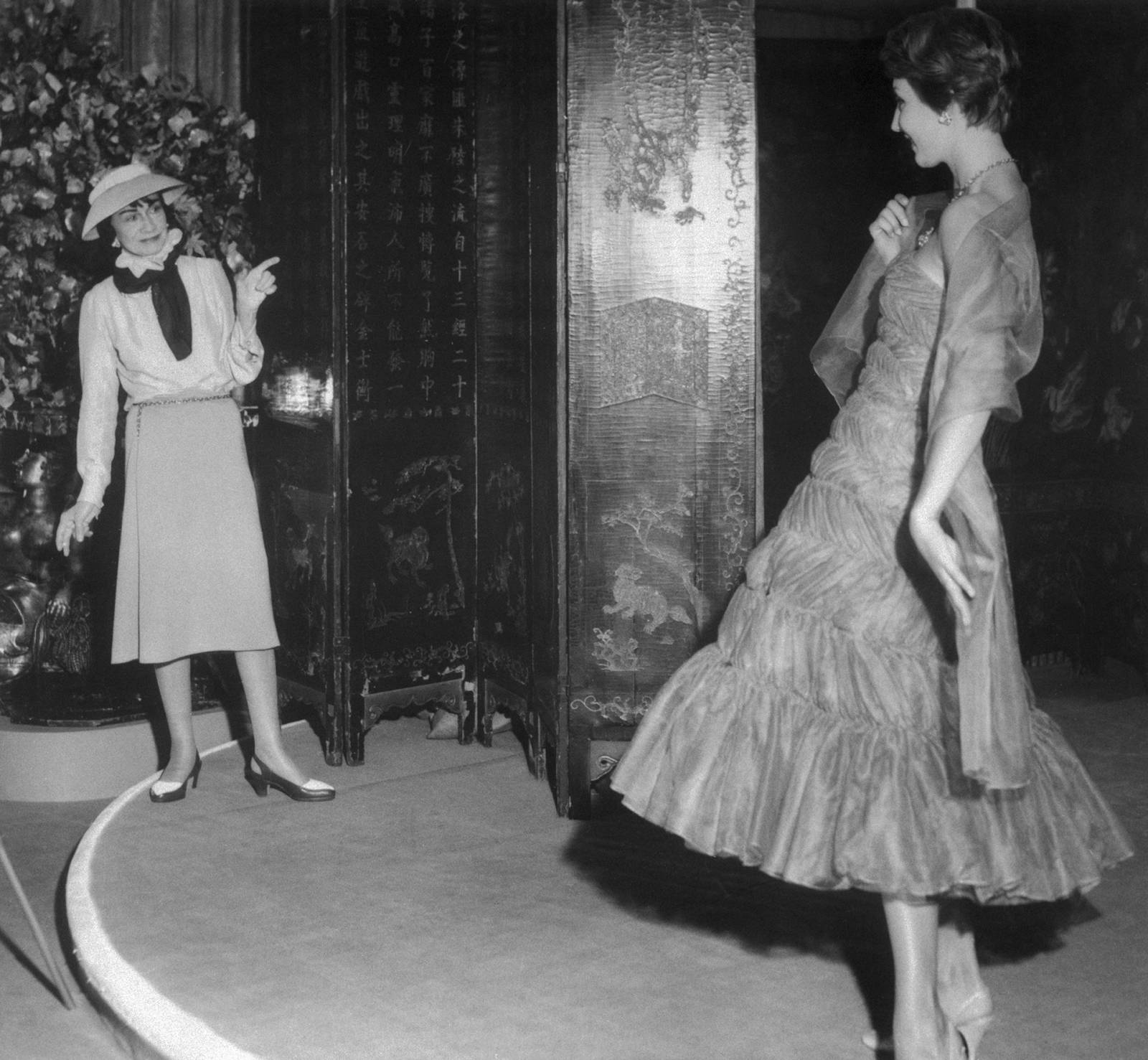 Coco Chanel patrząca na modelkę mającą na sobie szyfonową sukienkę z falbanami z jej kolekcji, 1957 rok (Fot. Getty Images)
