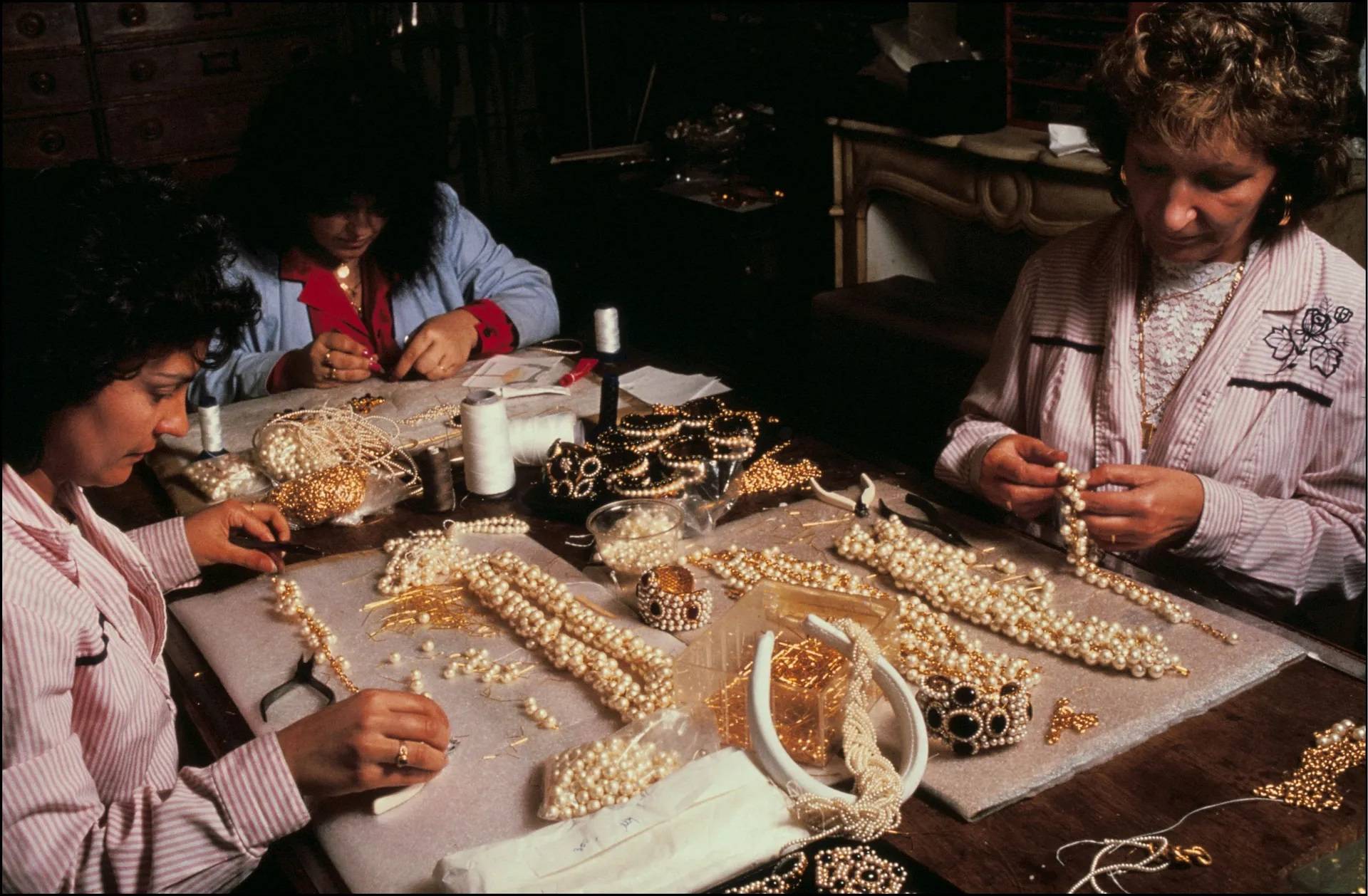 Pracownice atelier nawlekające kultową perłową biżuterię Chanel.