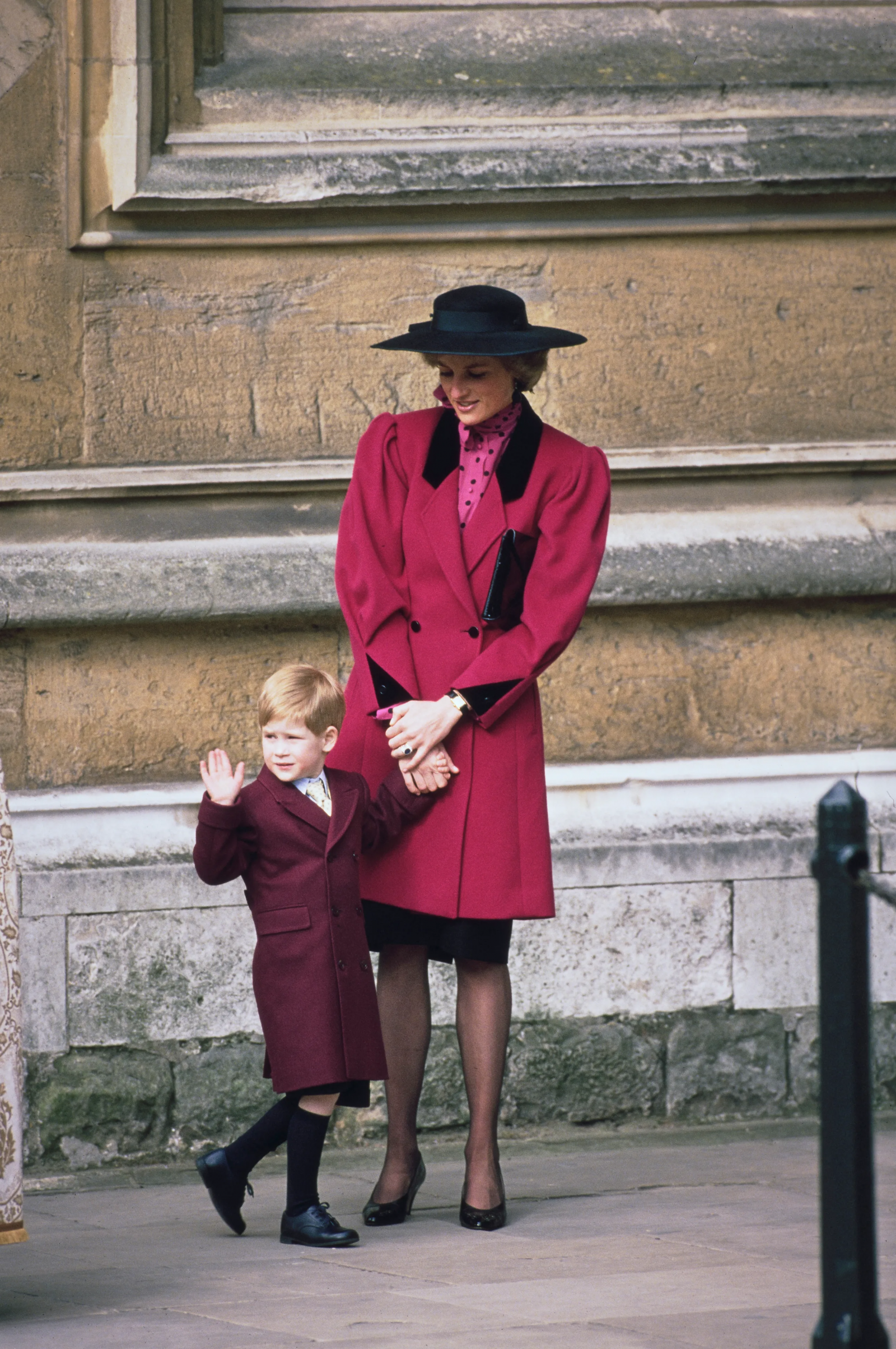 Księżna Diana ma na sobie czerwony płaszcz z czarnymi klapami i czarny kapelusz. Trzyma za rękę księcia Harry'ego, marzec 1989 r.