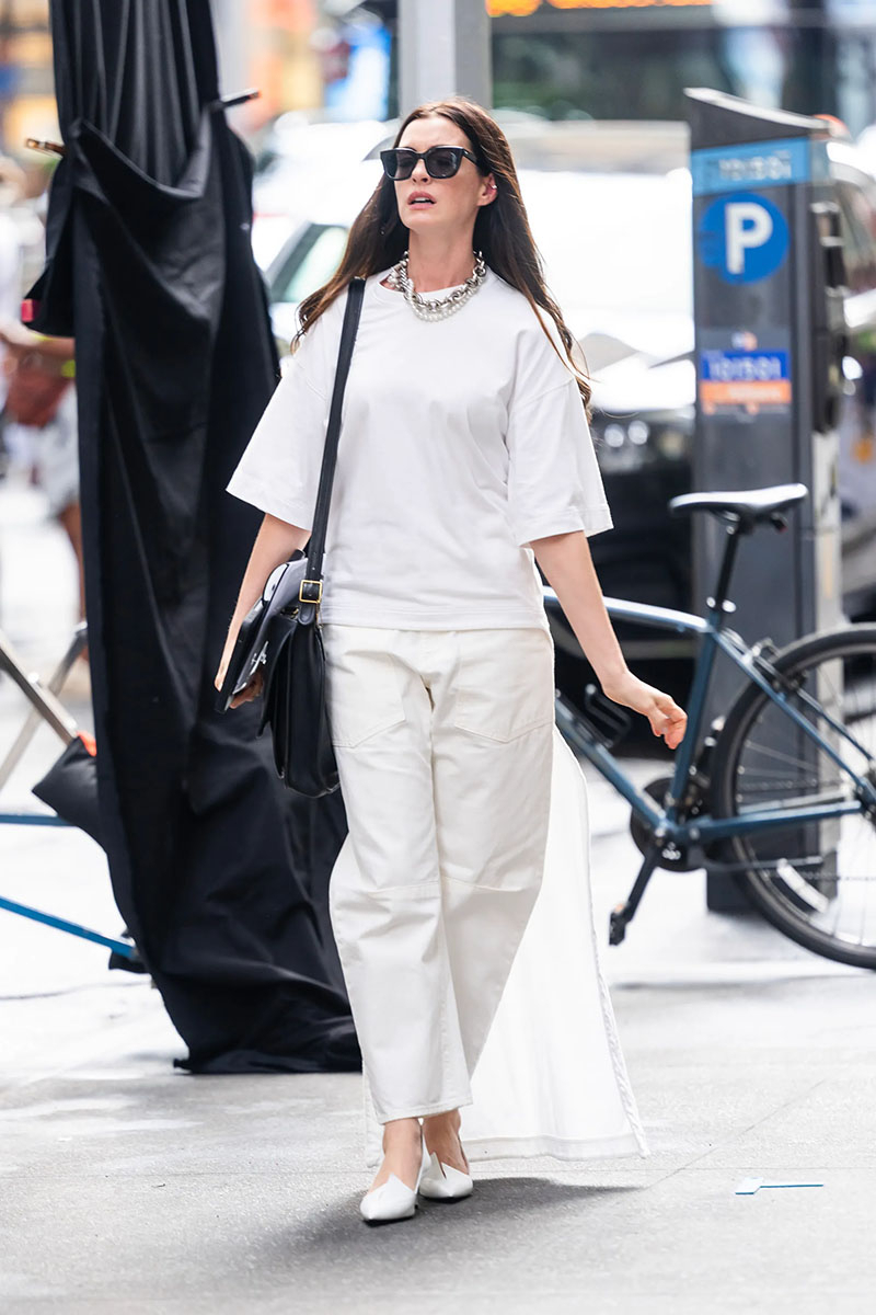 Anne Hathaway w białym total looku z czółenkami Prady i torebką Coach.