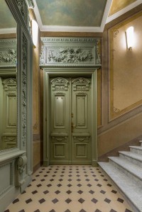 Reprezentacyjne drzwi wejściowe i rozrzeźbiona supraporta są zapowiedzią historycznych dekoracji, które można zobaczyć we wnętrzach apartamentów