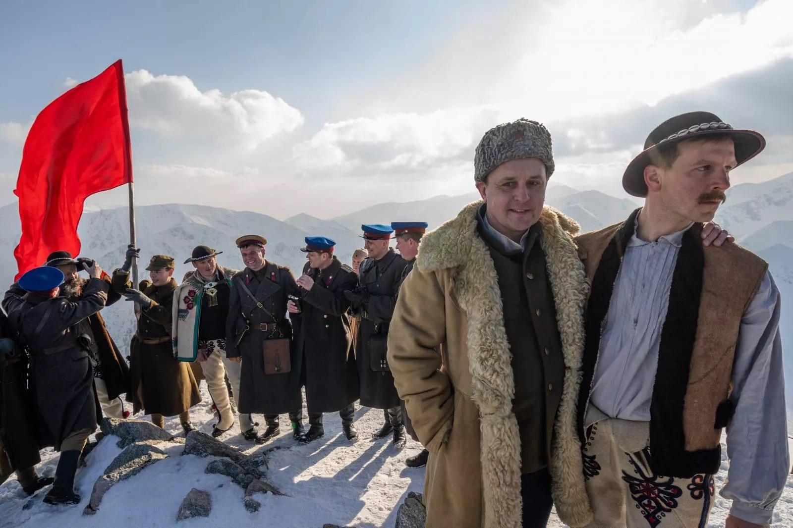 Scena z filmu "Biała odwaga", przedstawiająca postacie w historycznych strojach na górskiej szczycie z czerwonym flagą w tle.