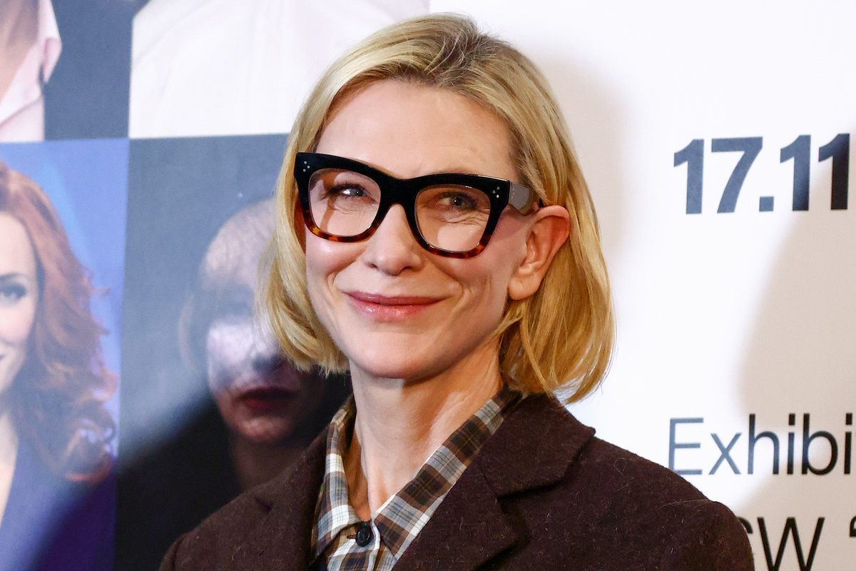 Cate Blanchett prezentuje w Łodzi elegancki garnitur damski w modnym odcieniu brązu na zimę 2025 roku. Ma na sobie również koszule w kratę i modne okulary korekcyjne.