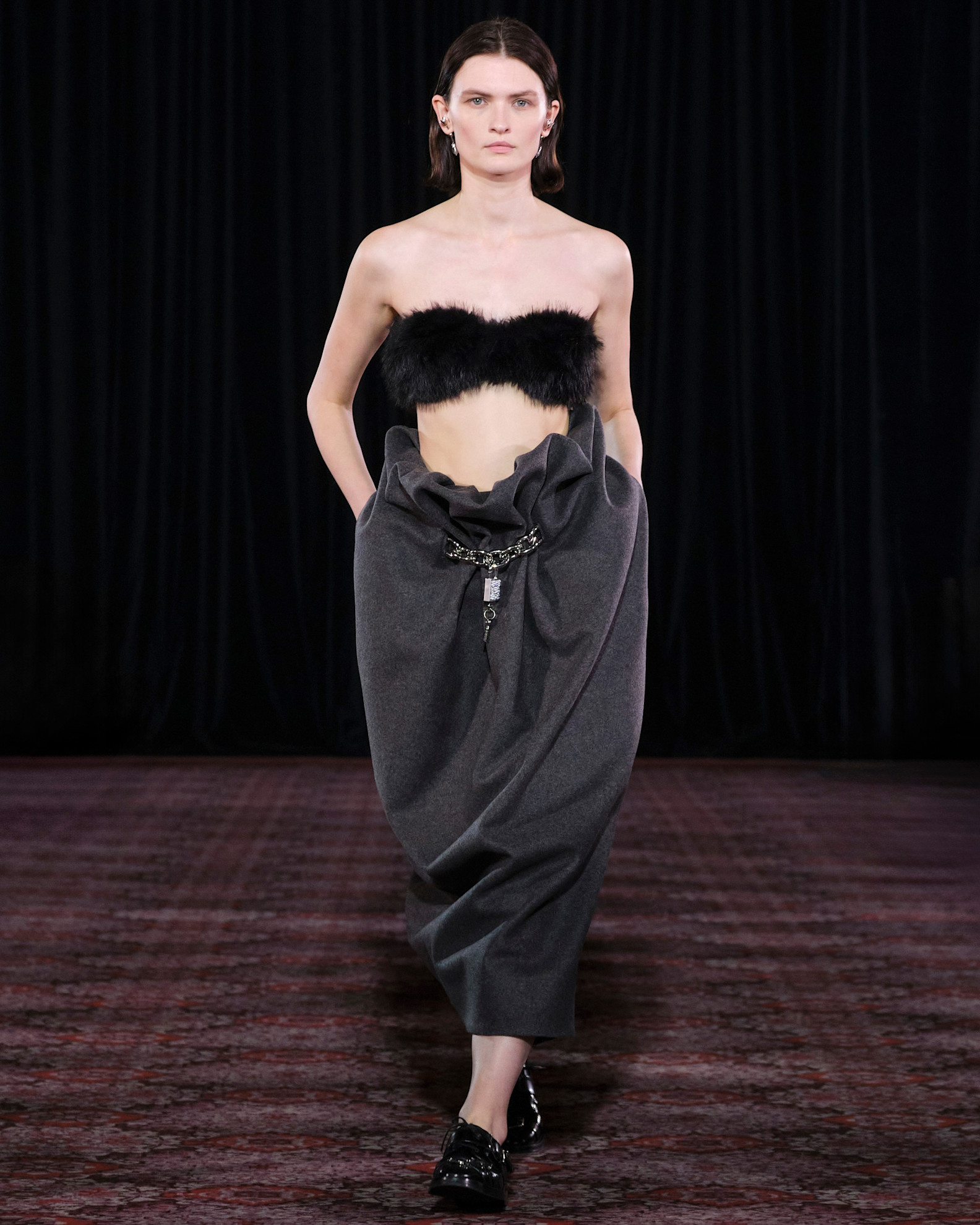 Modelka w wełnianej spódnicy i futrzanym topie prezentuje się na wybiegu w eleganckim otoczeniu.