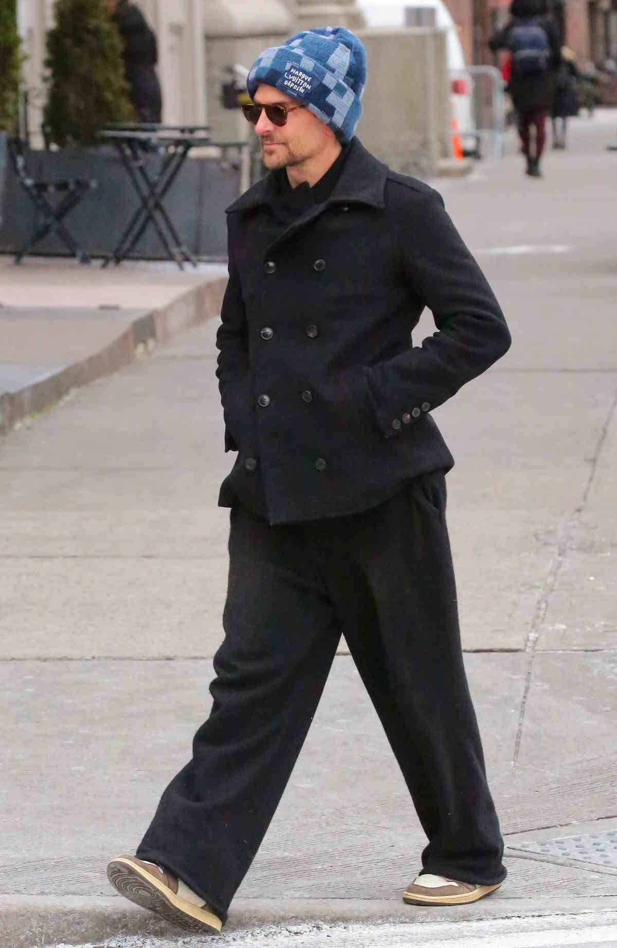 Stylizacja Bradleya Coopera_niebieska czapka Louis Vuitton, szerokie czarne spodnie i sneakersy.
