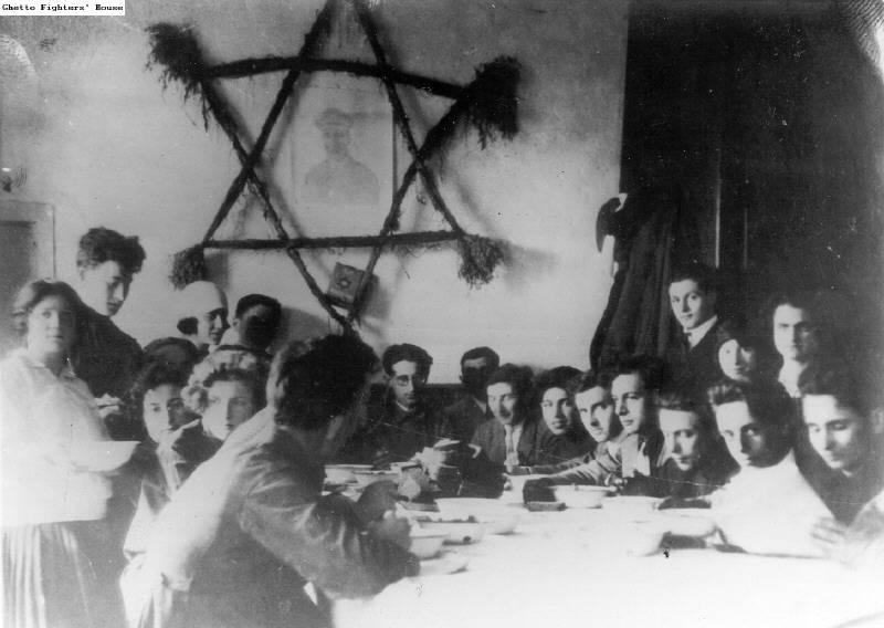 Posiłek w wigilię szabatu w pionierskiej farmie szkoleniowej (hachshara) ruchu He-Chaluts na Grochowie. Na ścianie wisi portret Josepha Trumpeldora otoczony dużą gwiazdą Dawida. Źródło: Ghetto Fighters House Archives
