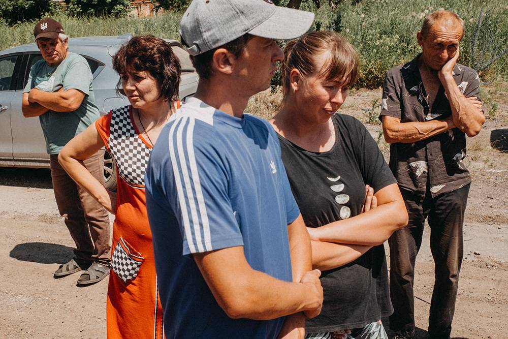Dowhenke, wieś w połowie drogi między Iziumem a Słowiańskiem, położona na wzniesieniu z otwartym widokiem na pola i główną drogę, stała się polem bitwy podczas rosyjskiej agresji na Ukrainę. Wszyscy z 540 mieszkańców uciekli, zostawiając swój dobytek, bydło, a czasem psy i koty. Po sześciu miesiącach nieustannych walk ani jeden dom nie pozostał nietknięty. Prawie rok po wyzwoleniu zaledwie 30 mieszkańców wróciło, aby odbudować swoje życie i domy, żyjąc na terenach silnie zaminowanych bez wody i prądu. na zdjęciu: Alina Bojko (2. od lewej) z mężem Pawłem (w środku) oczekują na dostawę pomocy humanitarnej (Fot. Wojciech Grzędziński)