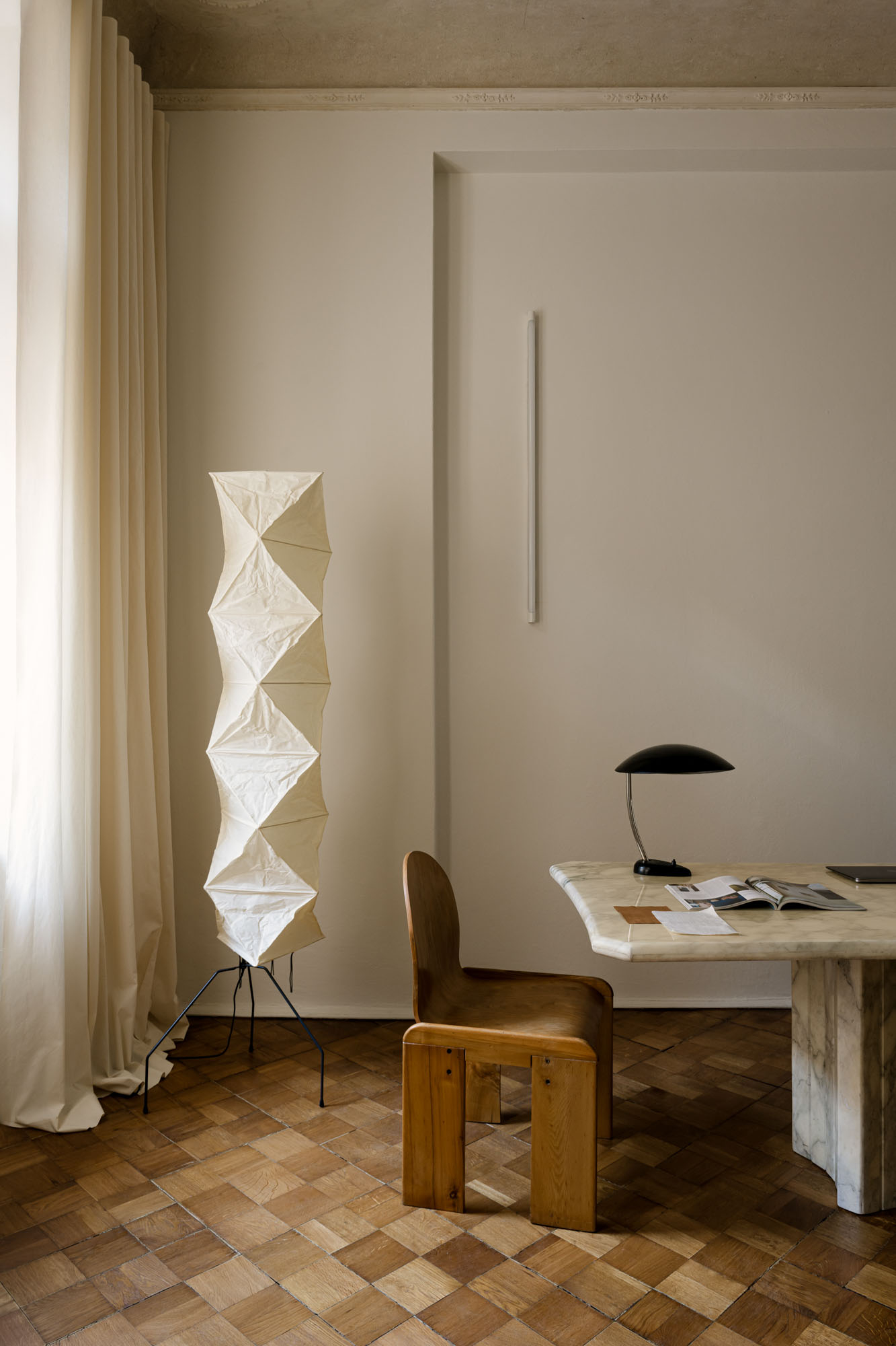 Minimalistyczne wnętrze z biurkiem, drewnianym krzesłem i lampą, obok stoi nowoczesna lampa podłogowa.
