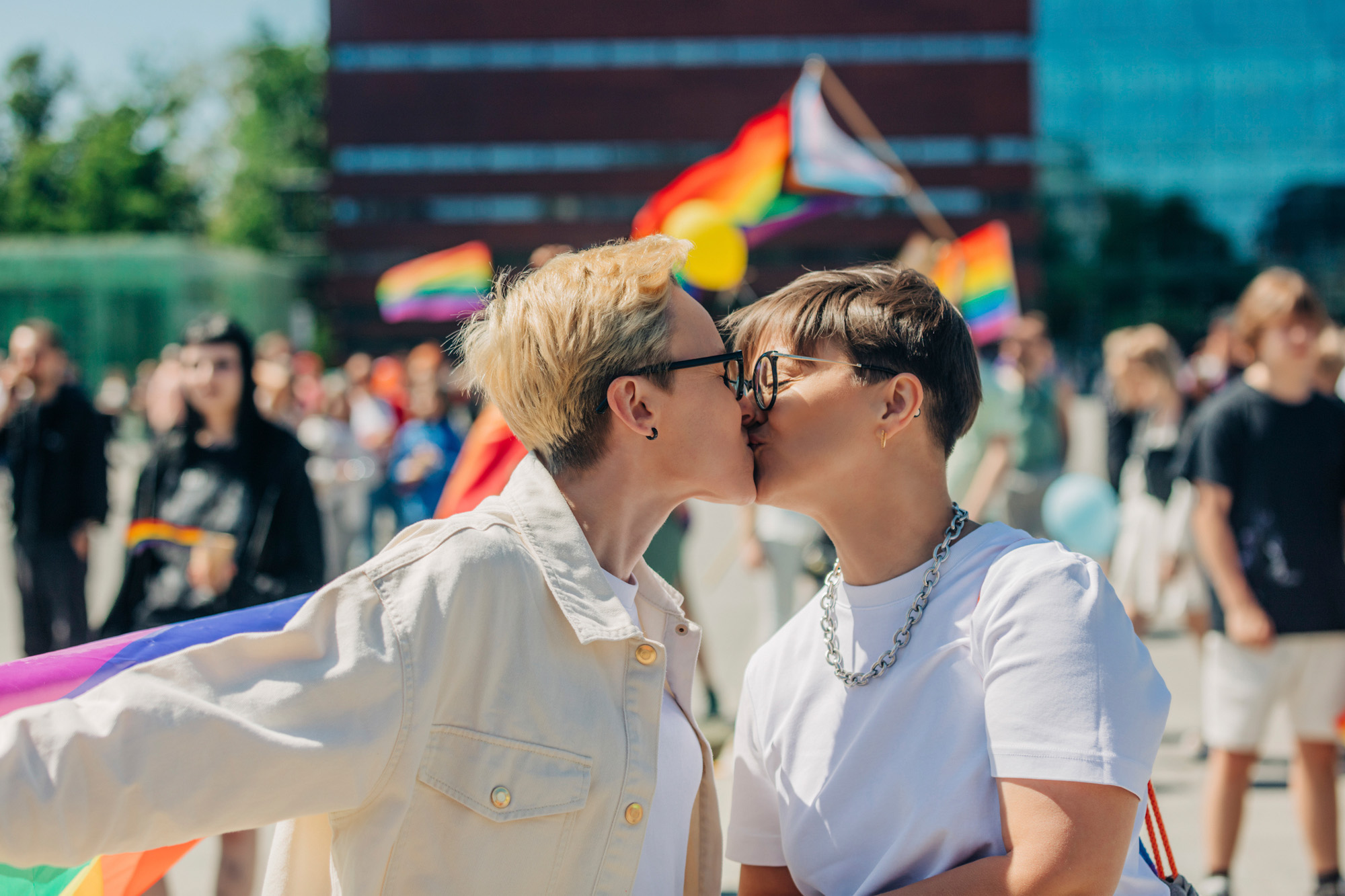 Para LGBT+ całuje się wśród tęczowych flag.