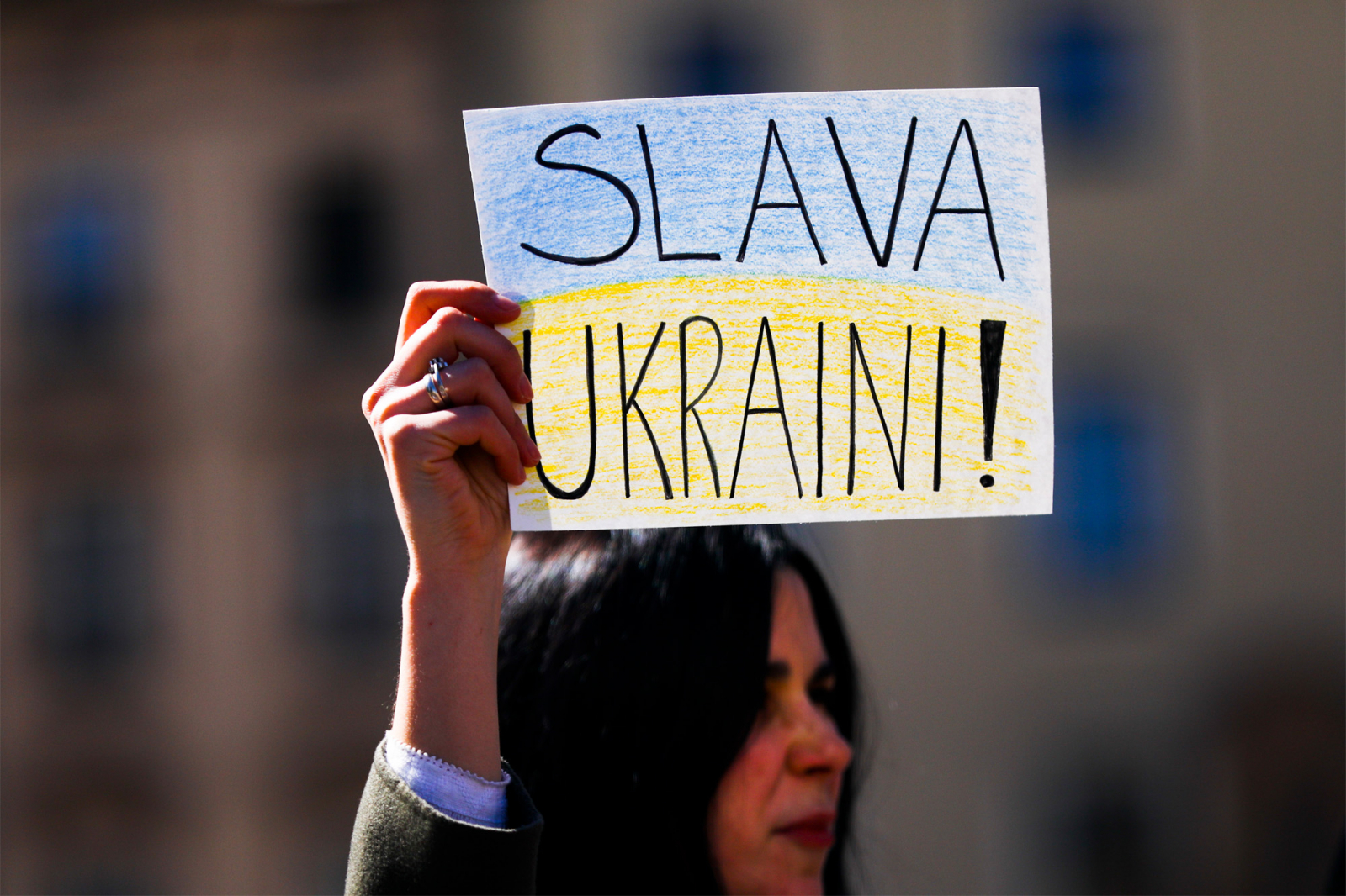 Osoba trzyma transparent z napisem "SLAVA UKRAINI!" na tle zamglonego miasta.