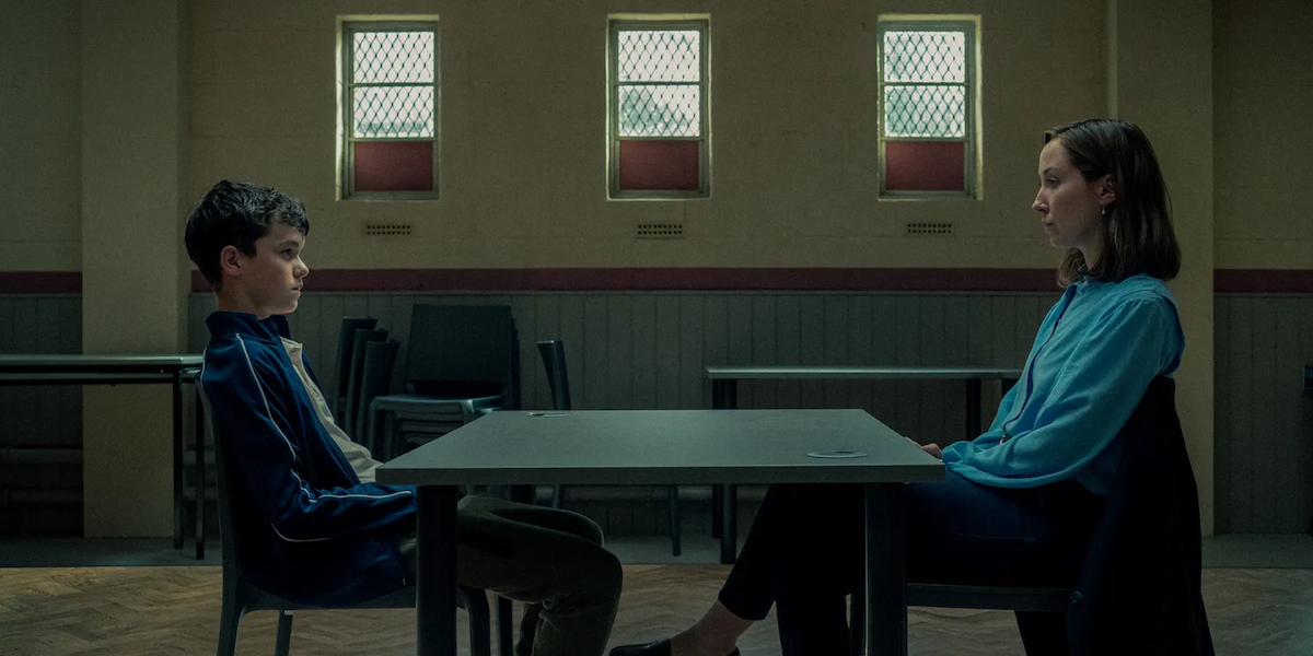 Aktor Owen Cooper i Erin Doherty w scenie z serialu Netflix „Dojrzewanie”, siedzą przy stole w minimalistycznym pomieszczeniu.