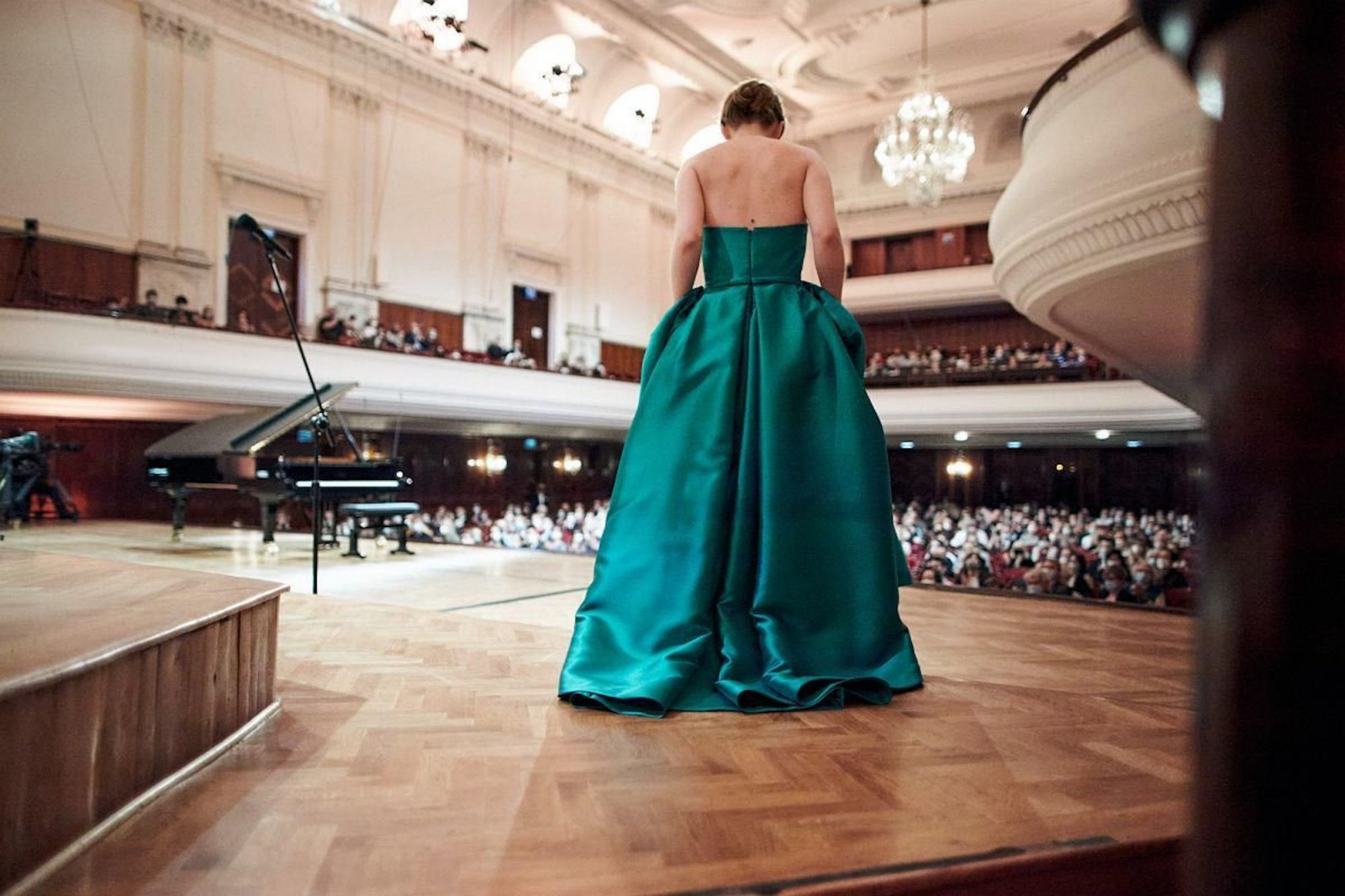 Występ w filharmonii, elegancka kobieta w zielonej sukni na scenie, a w tle fortepian. Polska produkcja „Pianoforte”.
