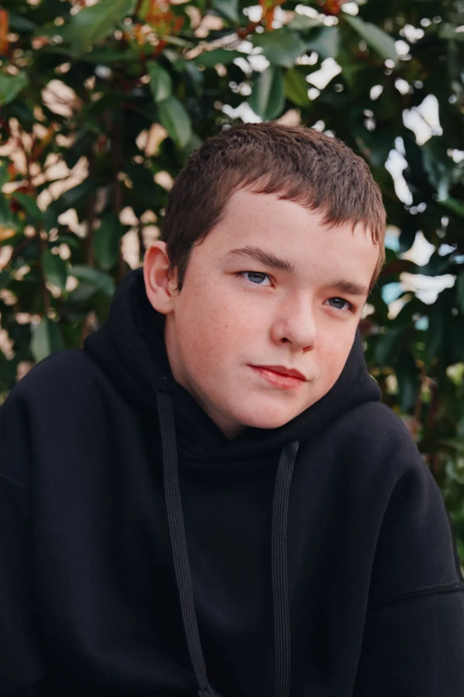 Aktor Owen Cooper, gwiazdor serialu Netflix „Dojrzewanie”, z zamyśloną miną na tle zieleni.
