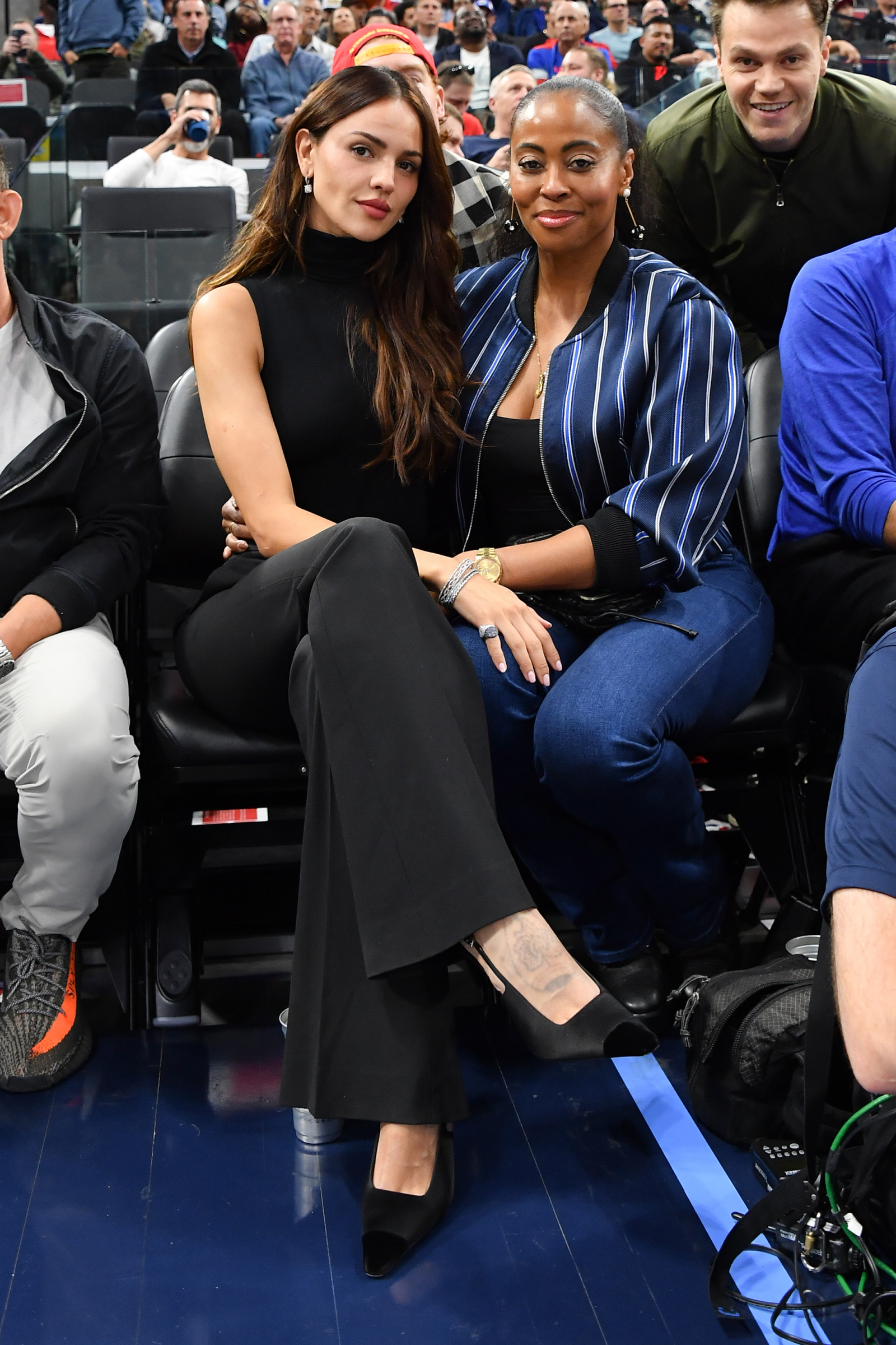 Eiza González i Nichelle Hines siedzą na trybunach, uśmiechając się wśród innych widzów.