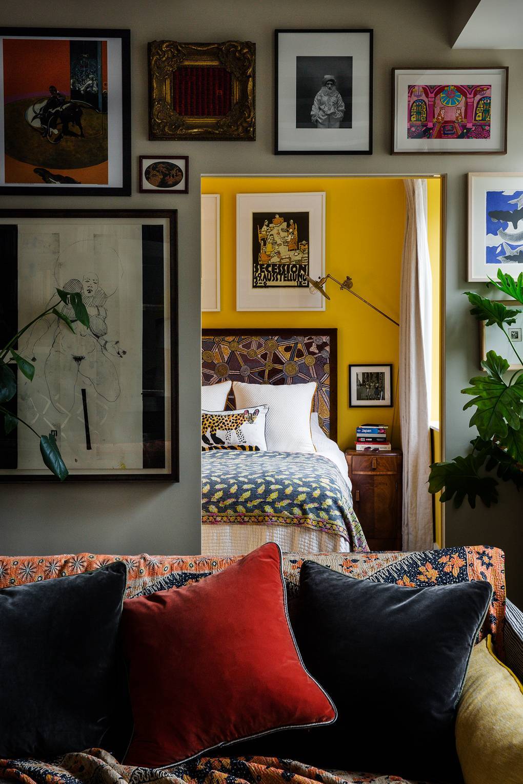  Widok z salonu do sypialni: żółta ściana pomalowana farbą Farrow&Ball w kolorze „Babouche”, poduszka z autorskim printem artystki Machiko oraz zagłowie łóżka pokryte tkaniną Pierre Frey. (Fot. Owen Gale dla House&Garden)
 