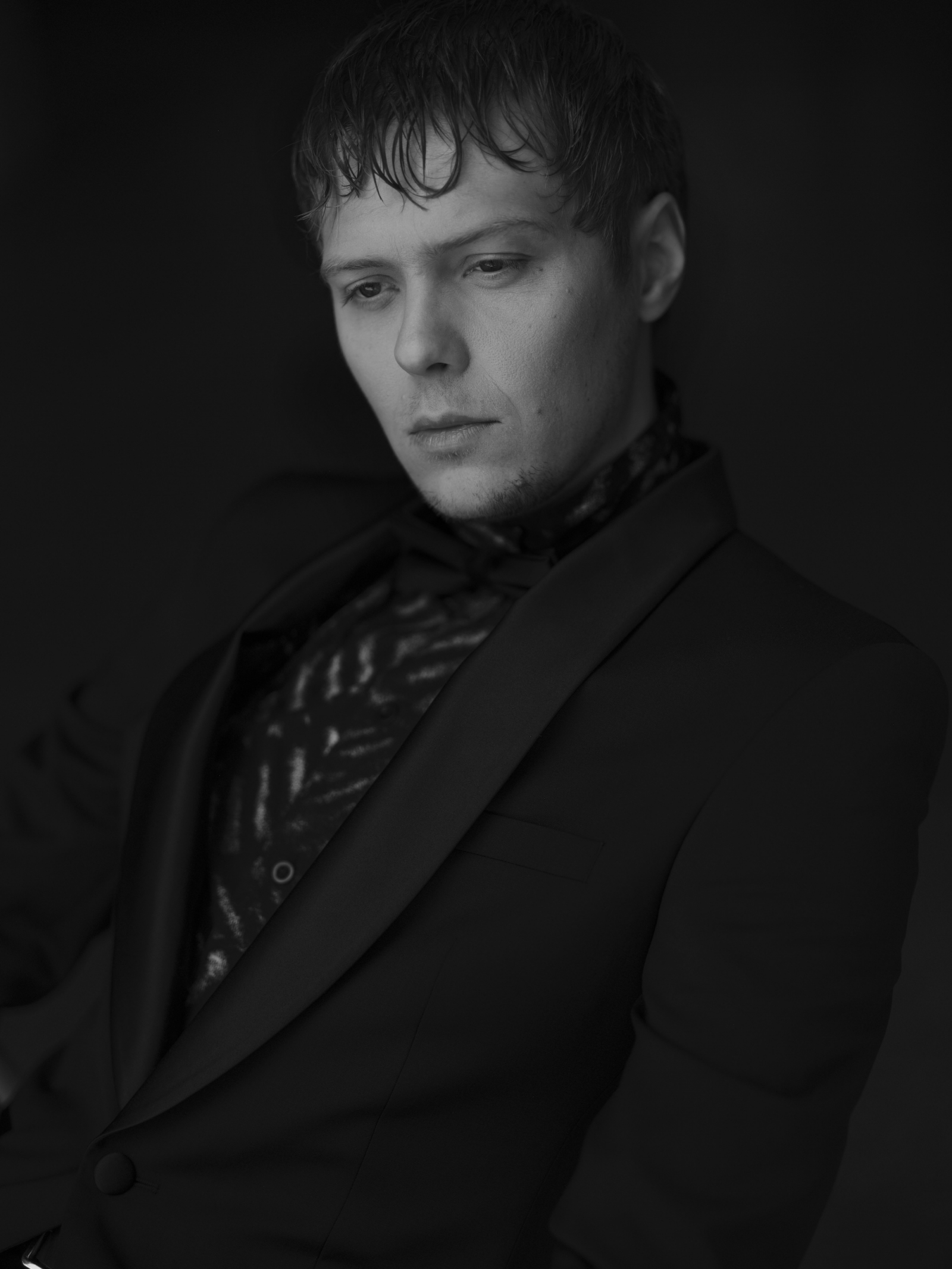 Jakub Gierszał w eleganckim garniturze, z zamyślonym wyrazem twarzy, kontrastujący z monochromatycznym tłem.
