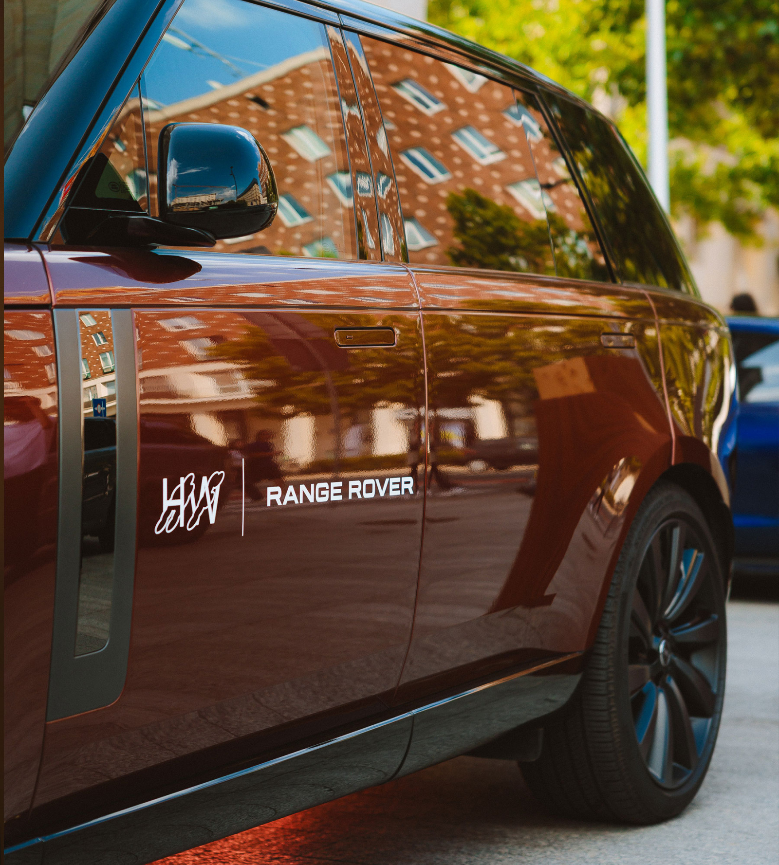 Luksusowy samochód marki Range Rover w kolorze brązowym, z widocznym logo oraz odbiciem otoczenia na karoserii.