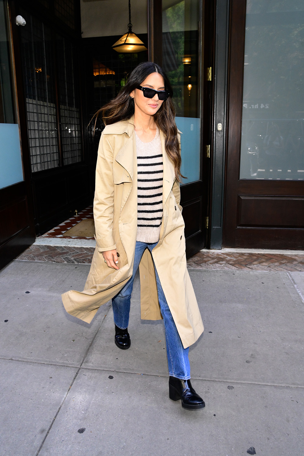 Olivia Munn w beżowym płaszczu, czarnych botkach i jeansach, spaceruje po ulicy.