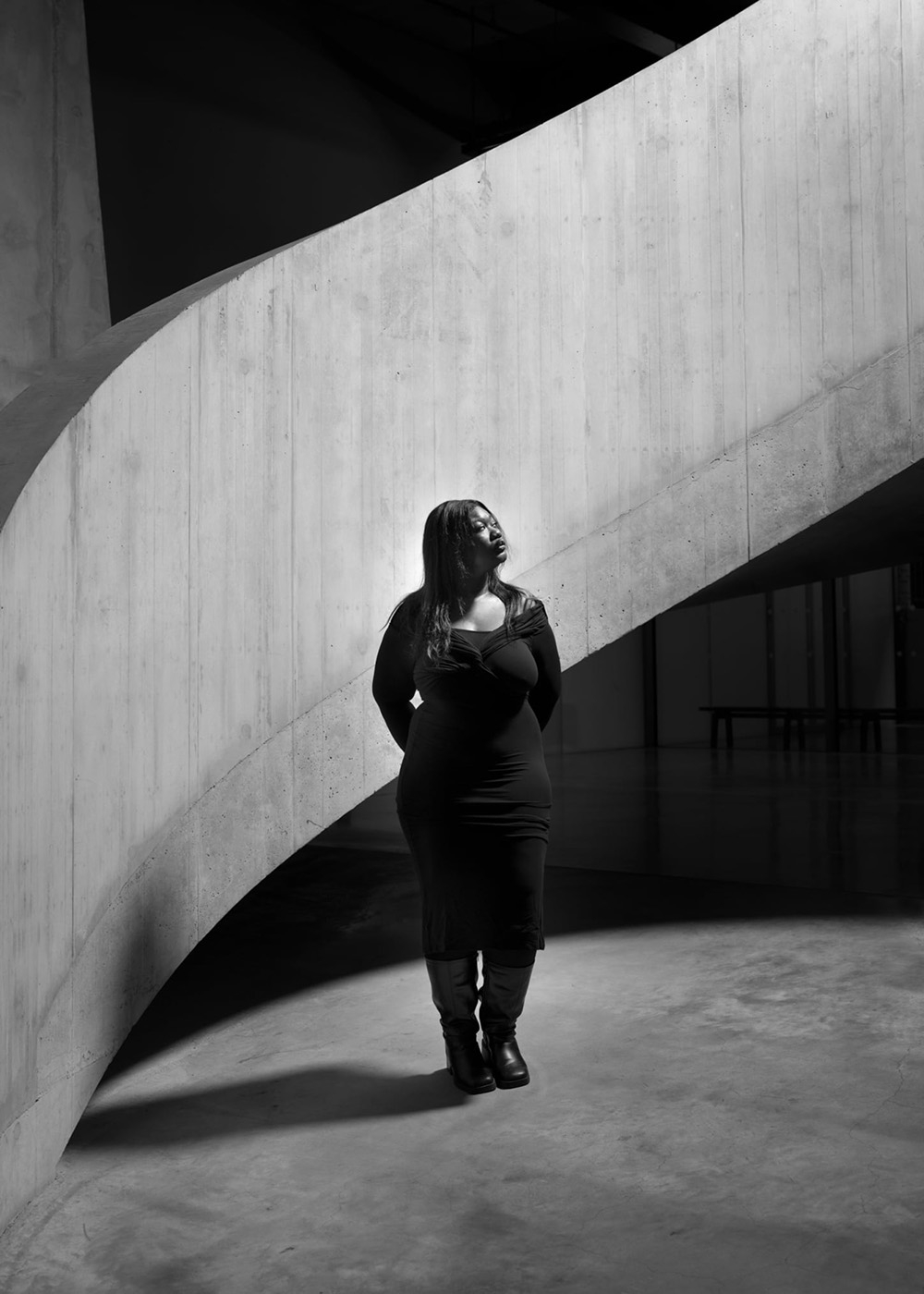 Artystka Crystalmess stojąca na tle przestrzennej, betonowej konstrukcji w monochromatycznym ujęciu.