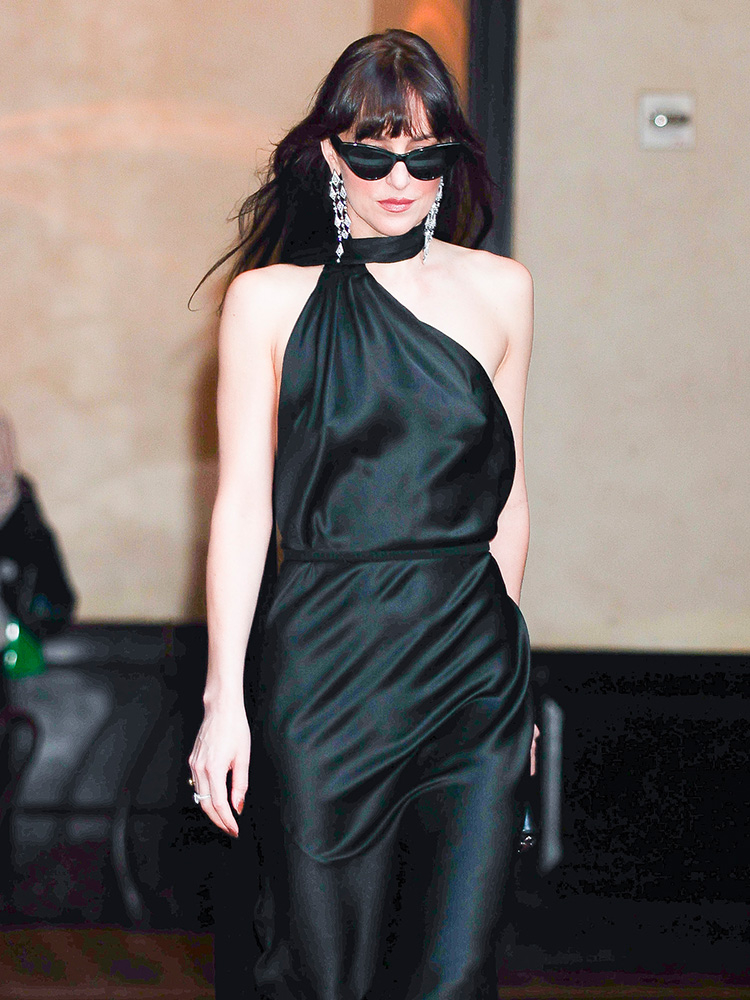 Dakota Johnson w czarnej sukience na wesele, z okularami przeciwsłonecznymi i długimi kolczykami, prezentuje elegancki wygląd.