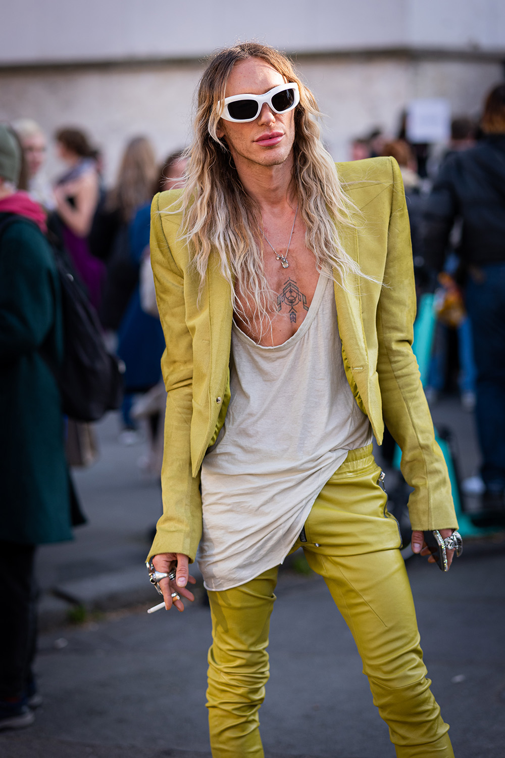 Tyrone Dylan Susman w jaskrawym, żółtym stroju na ulicy, trzyma papierosa, stylizując się na modnego.