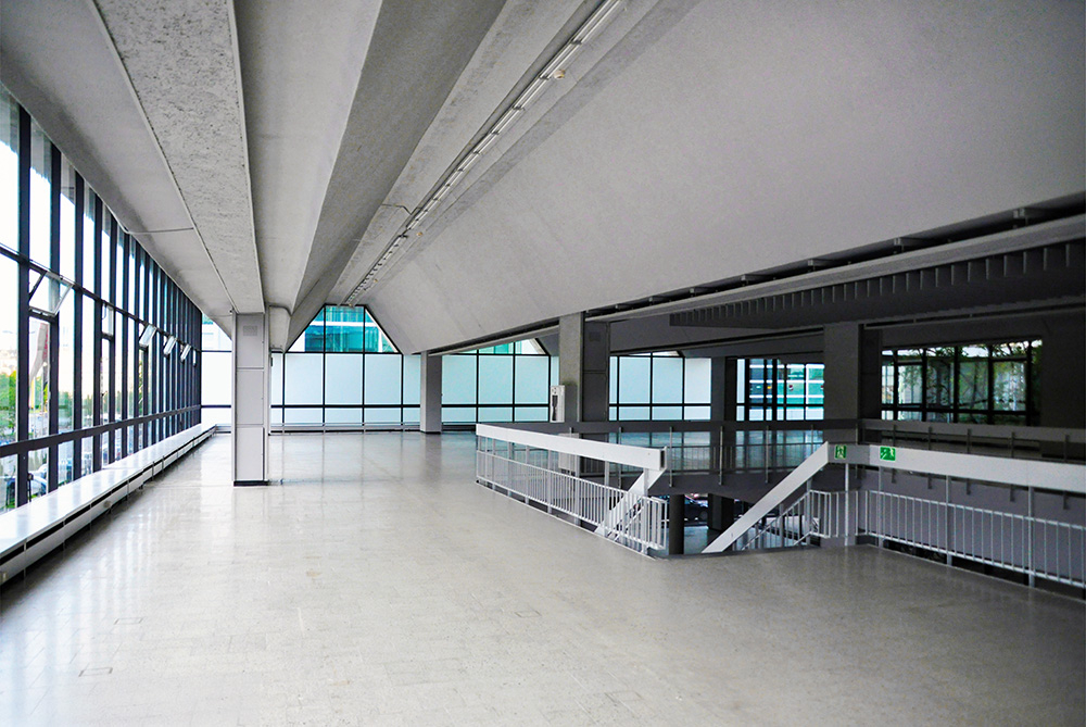 Przestronna wnętrze z dużymi oknami, nowoczesna architektura, betonowe i metalowe detale, brak mebli.
