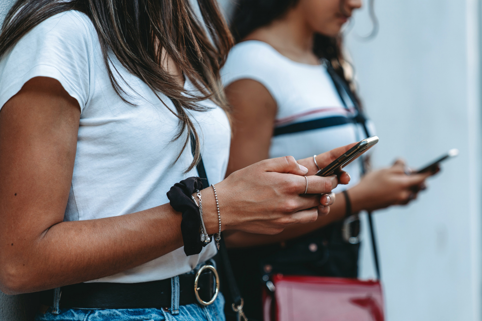 Dwóch młodych ludzi stoi obok siebie, korzystając z telefonów komórkowych. Jeden z nich nosi białą koszulkę, a drugi ma na sobie koszulkę z paskami.
