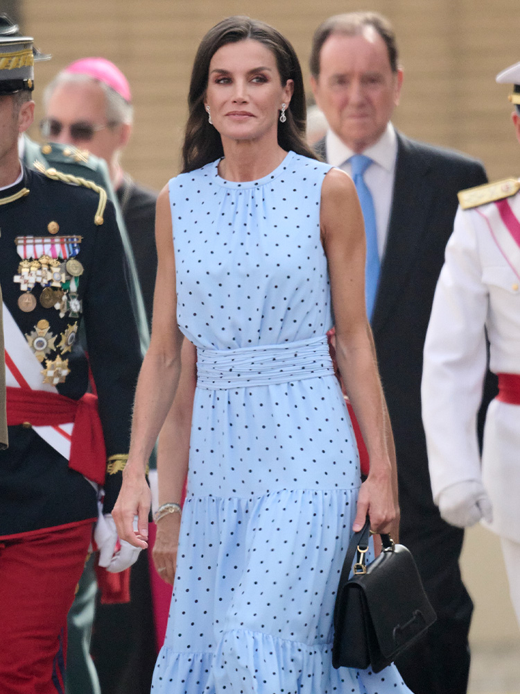 Królowa Letycja w niebieskiej sukience w groszki, idzie w towarzystwie elegancko ubranych mężczyzn.