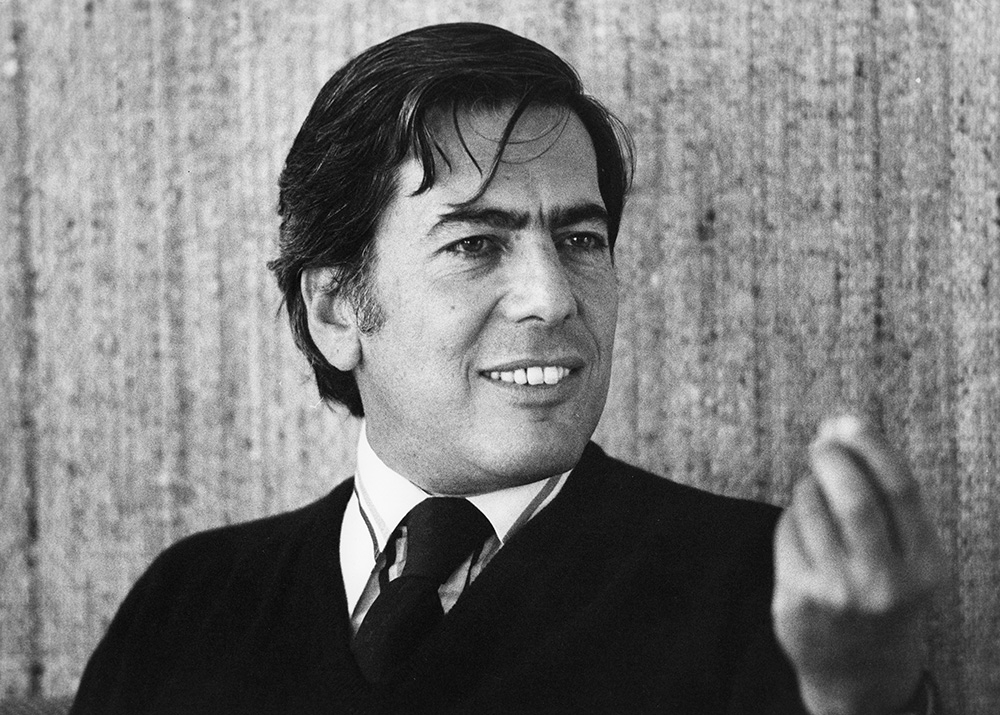 Mario Vargas Llosa, znany pisarz, uśmiecha się i gestykuluje w czarnobiałym portrecie.