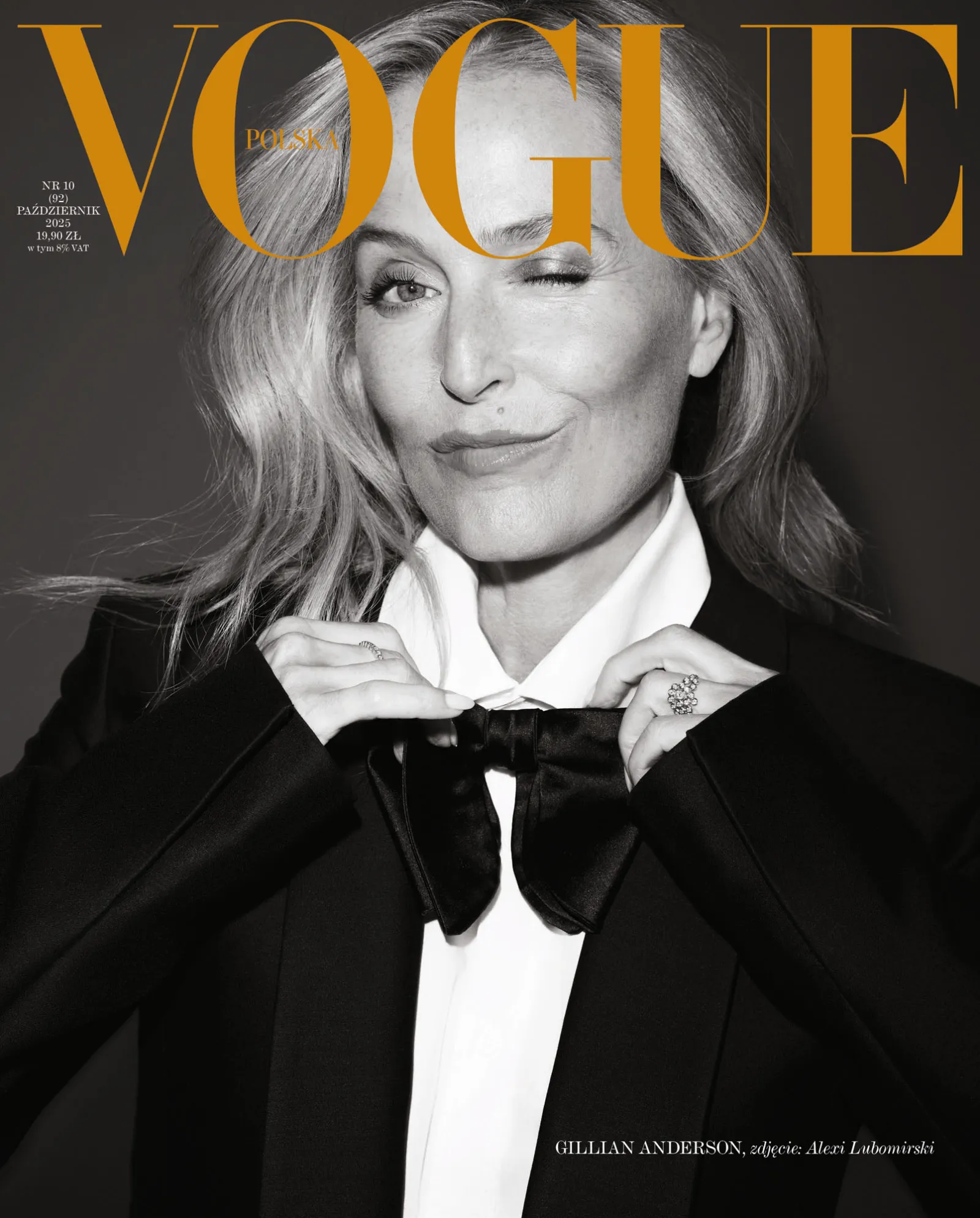 Na okładce "Vogue Polska" znajduje się kobieta w eleganckim czarnym garniturze, z kokardą w białej koszuli, uśmiechająca się.