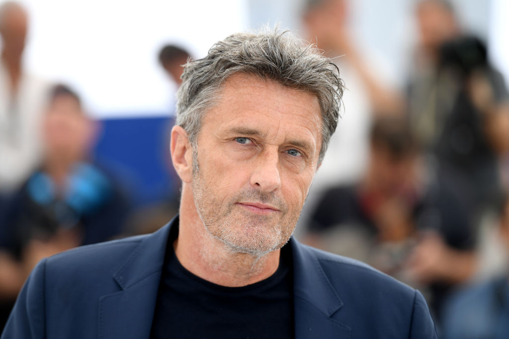 Paweł Pawlikowski podczas wydarzenia filmowego, na tle rozmytej grupy ludzi i aparatów.
