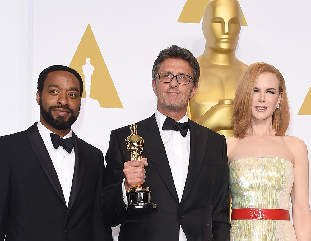 Paweł Pawlikowski stoi z Oscarami, obok niego dwóch innych uczestników uroczystości, w eleganckich strojach.