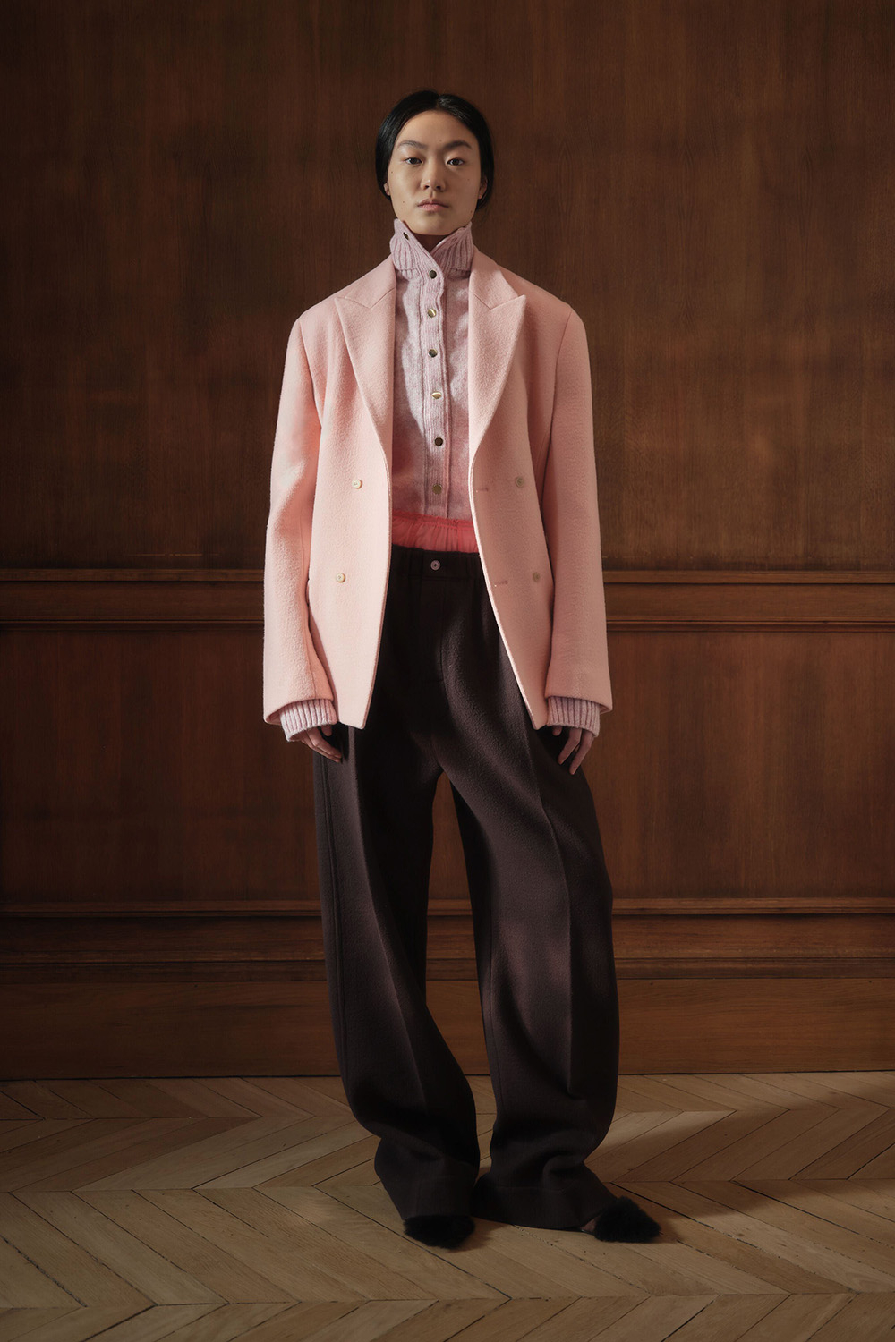 Modelka w różowej marynarce i brązowych spodniach prezentuje elegancki look od Carven.