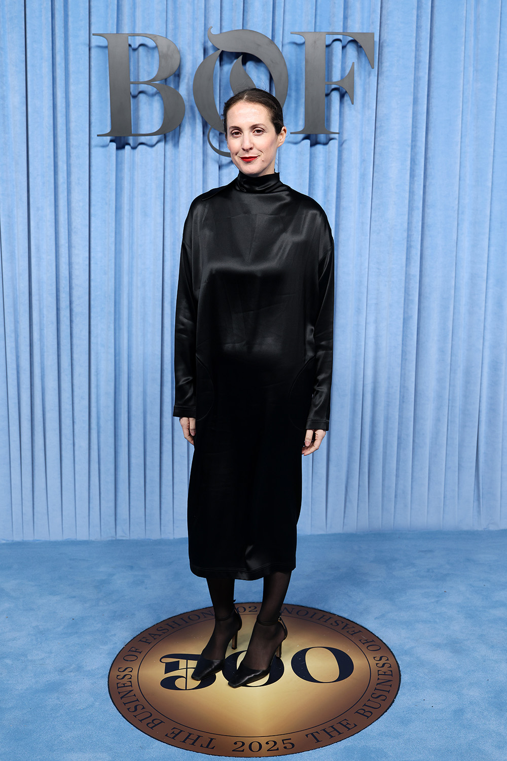 Kobieta w czarnej, długiej sukience stoi na okrągłej platformie z logo BOF na niebieskim tle.