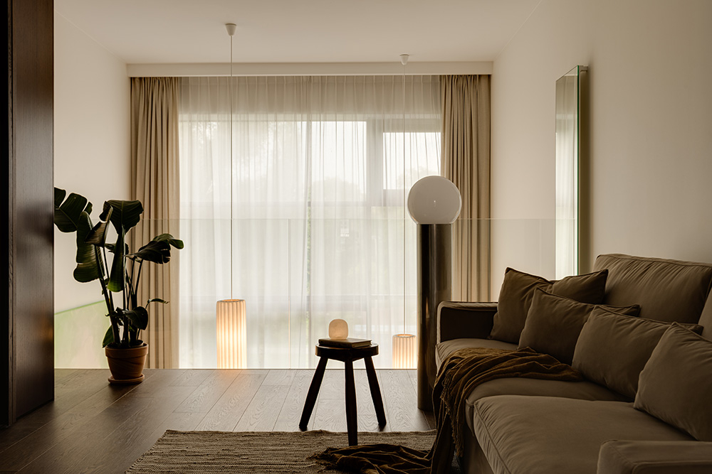 Nowoczesny salon z jasnymi zasłonami, rośliną, sofą i designerskimi lampami. Przytulny, minimalistyczny wystrój.