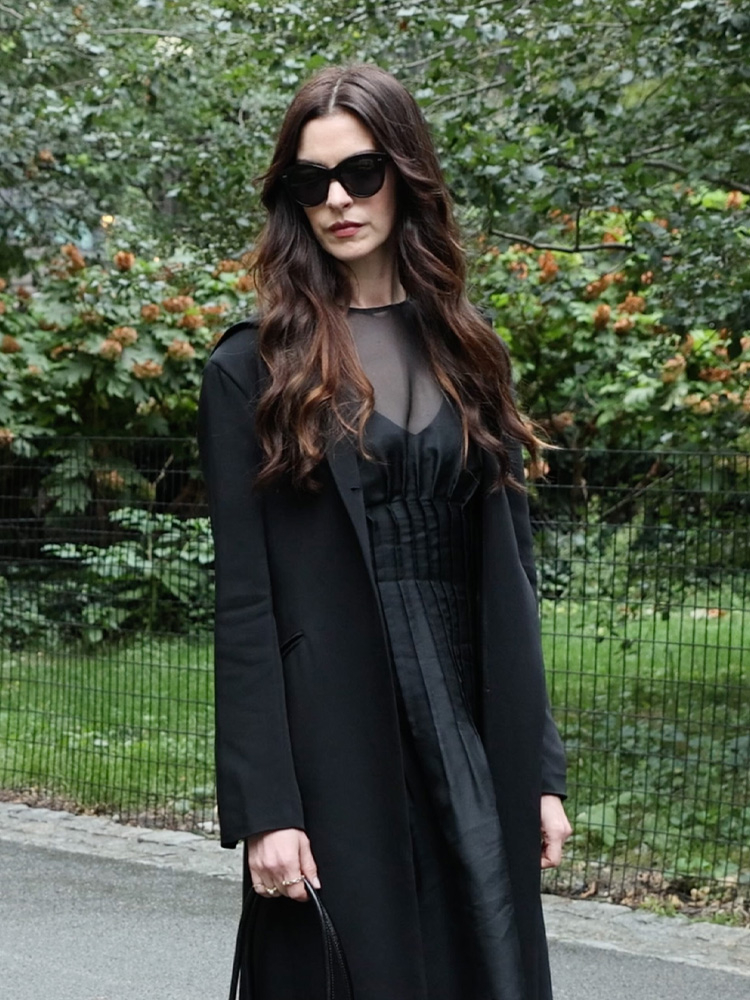 Anne Hathaway w długiej czarnej sukience i okularach przeciwsłonecznych, pozująca na ulicy.