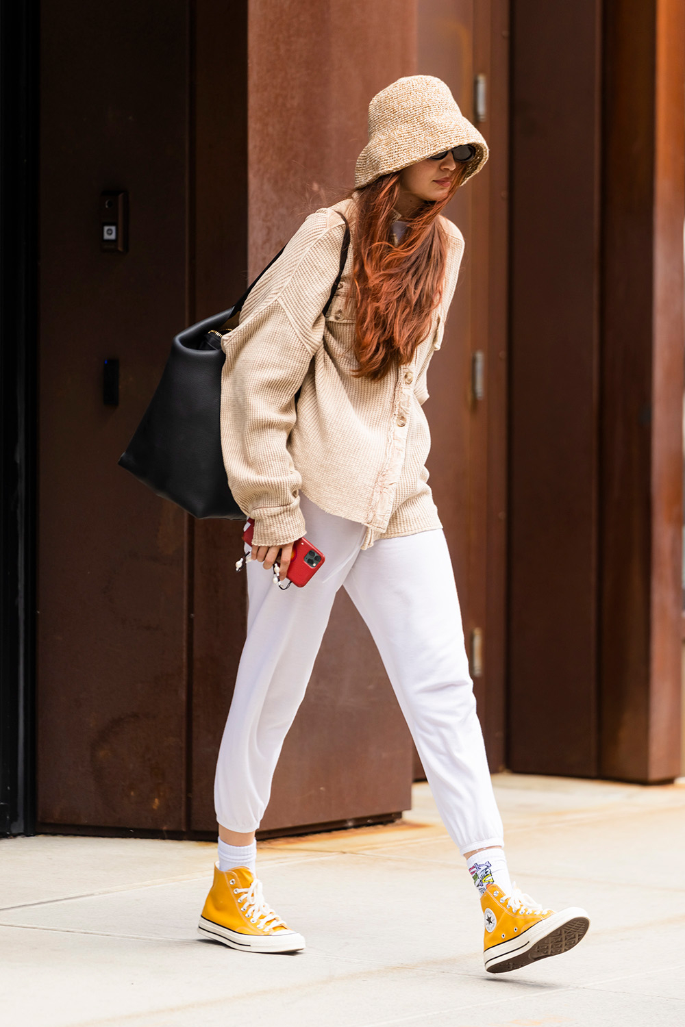 Gigi Hadid w białych spodniach i beżowej bluzie, nosi żółte tramki i plecak.