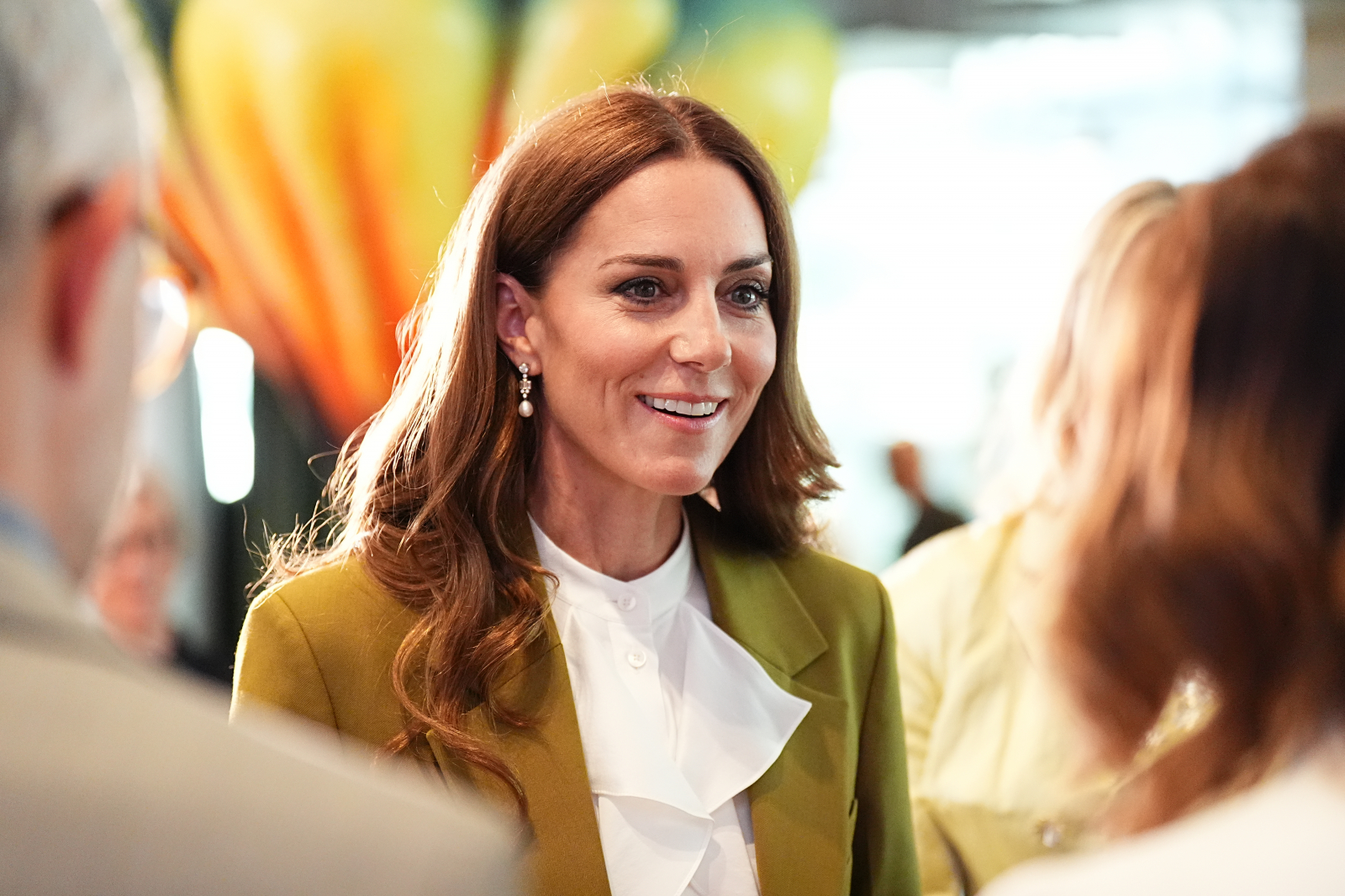 Księżna Kate w eleganckiej stylizacji, uśmiecha się podczas rozmowy z innymi uczestnikami wydarzenia.
