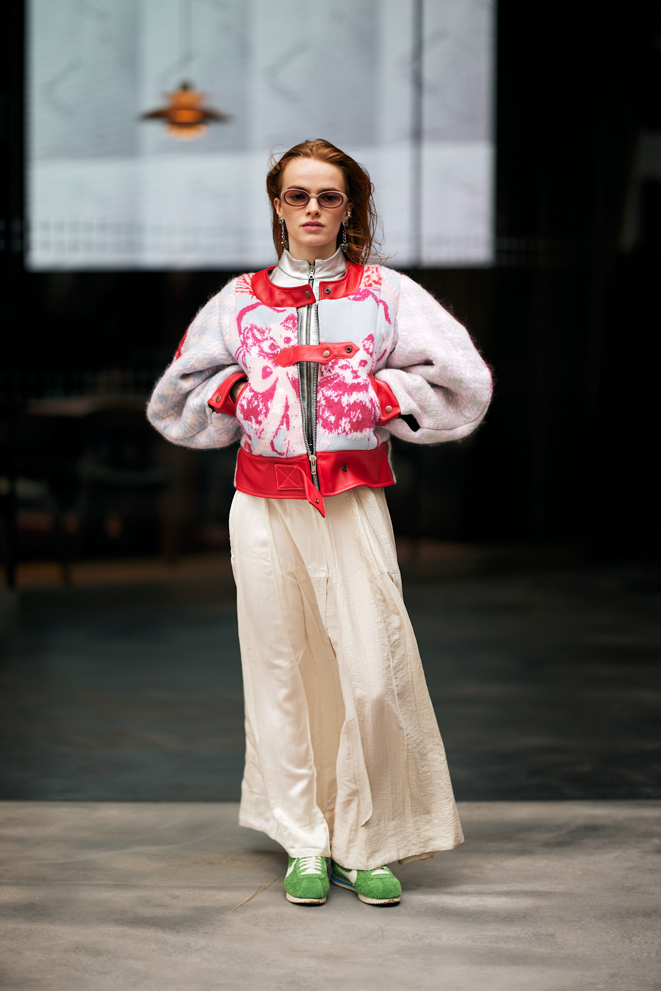 Modelka w różowej kurtce z oversized rękawami i białych spodniach, uzupełniona zielonymi sneakersami.