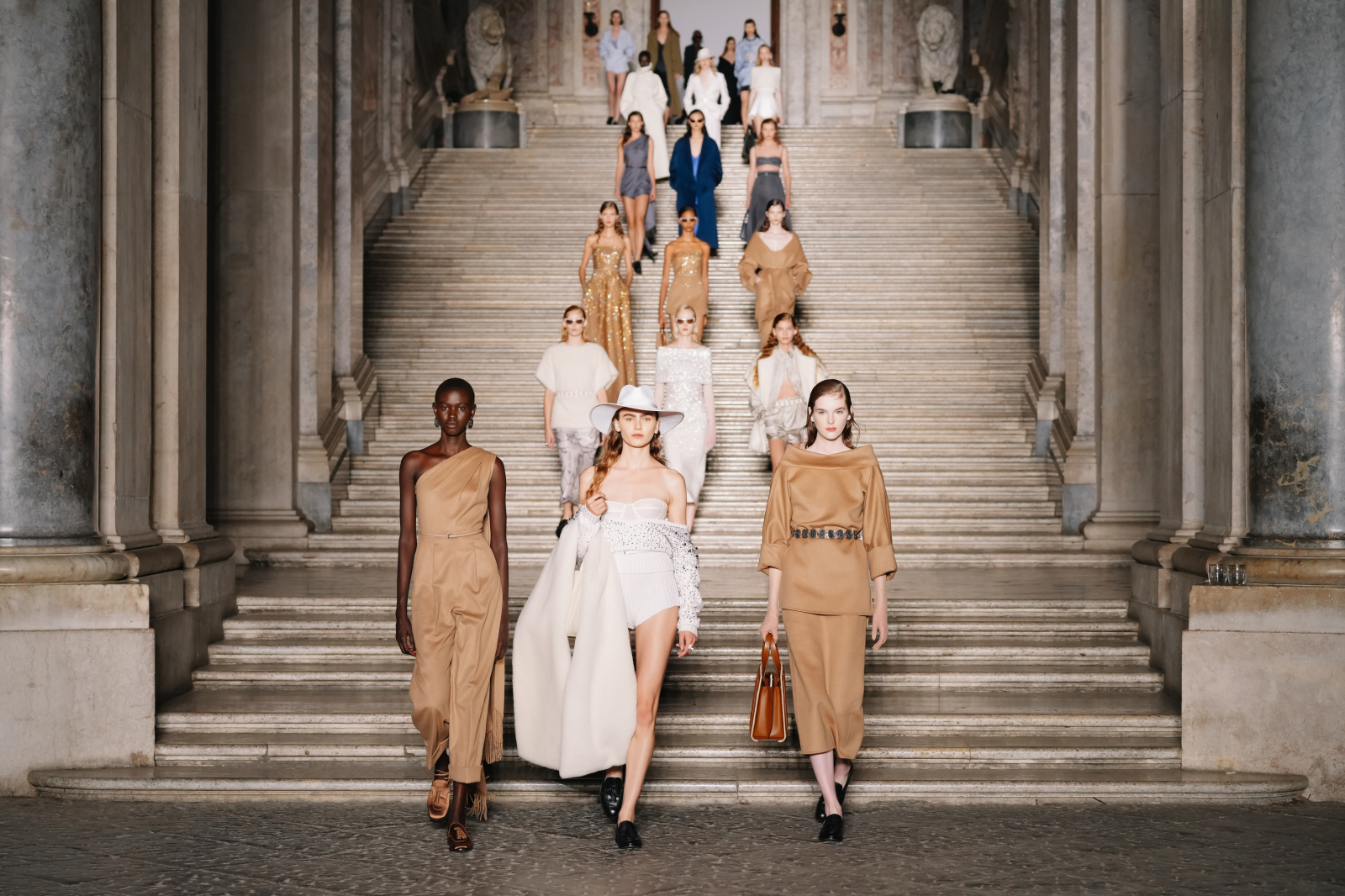 Modelki w kreacjach Max Mara Resort 2026 prezentują się na schodach, otoczeni elegancką architekturą.