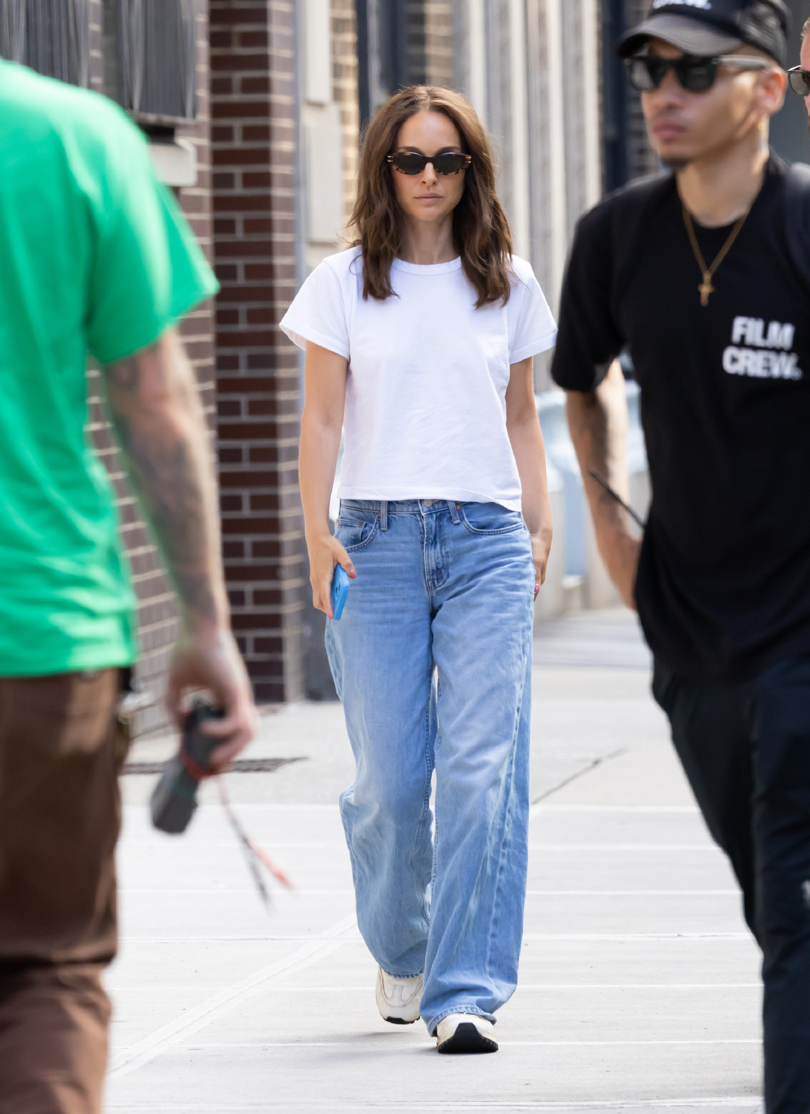 Natalie Portman w białym T-shircie i jeansach spaceruje po ulicy, w okularach przeciwsłonecznych.