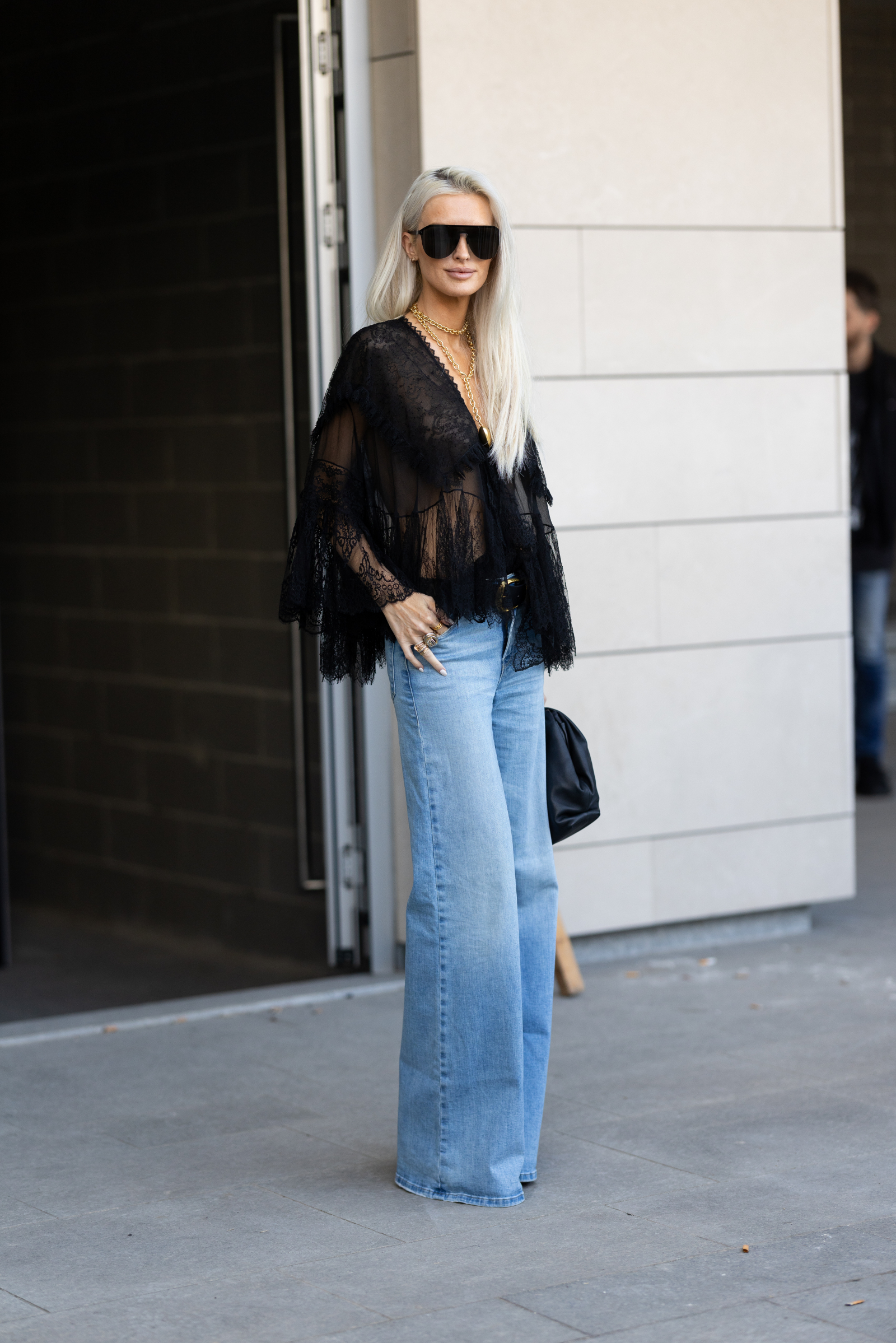 Kobieta w czarnej koszuli damskiej i jeansach bootcut stoi przy drzwiach, z torebką w ręku.