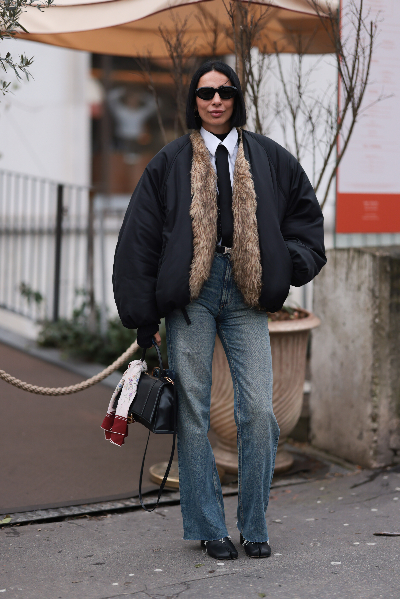 Kobieta w czarno-beżowej kurtce i białej koszuli nosi jeansy bootcut oraz czarne botki.
