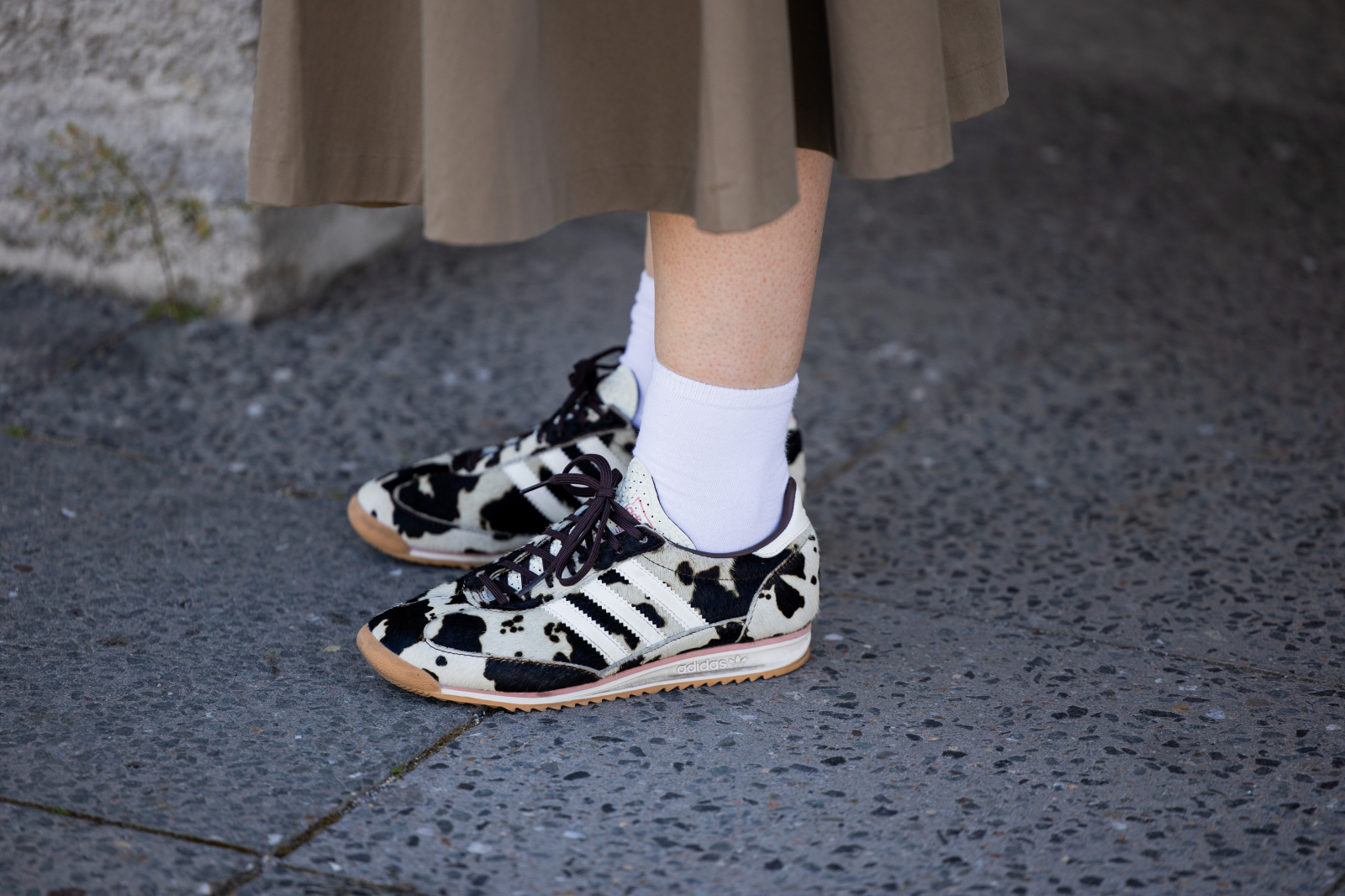 Sneakersy w krowie łaty zestawione z białymi skarpetkami, stojące na szarej nawierzchni.