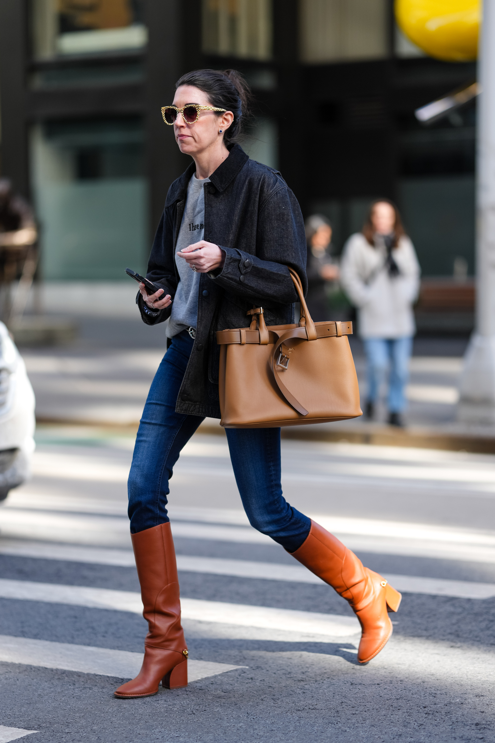 Kobieta w skinny jeans i kozaki, trzymając torebkę, przechodzi przez ulicę.