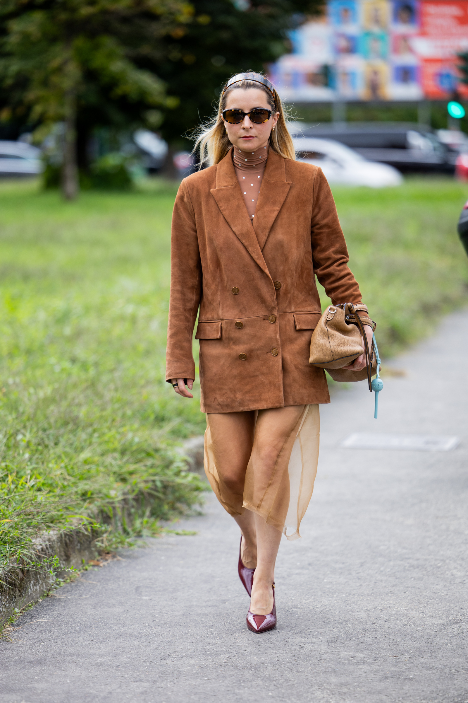 Kobieta w brązowej skórzanej marynarce idzie ulicą, niosąc torebkę, w połączeniu z elegancką spódnicą.