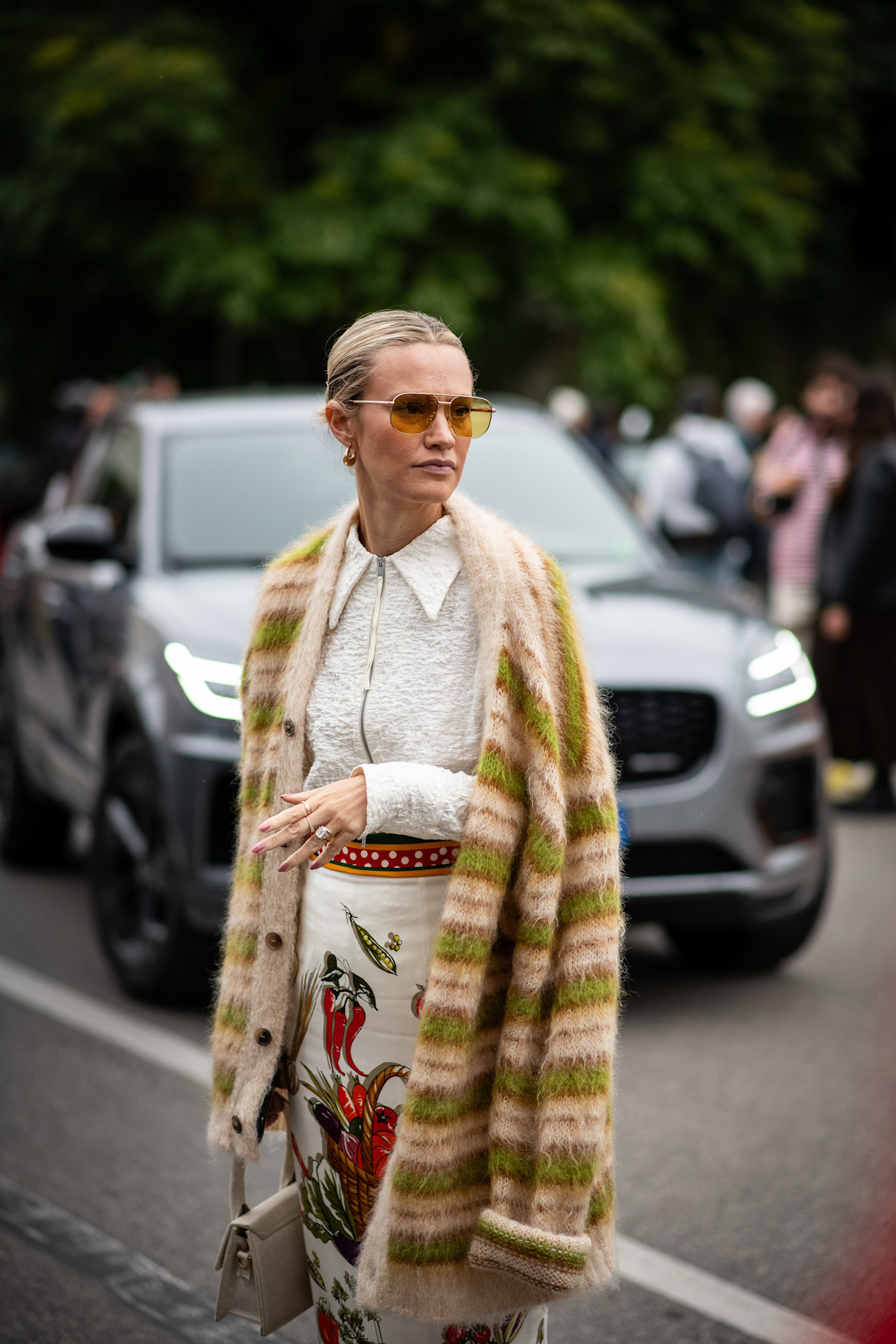 Stylowo ubrana kobieta w obszernym kardiganie i eleganckiej spódnicy z kolorowym nadrukiem.