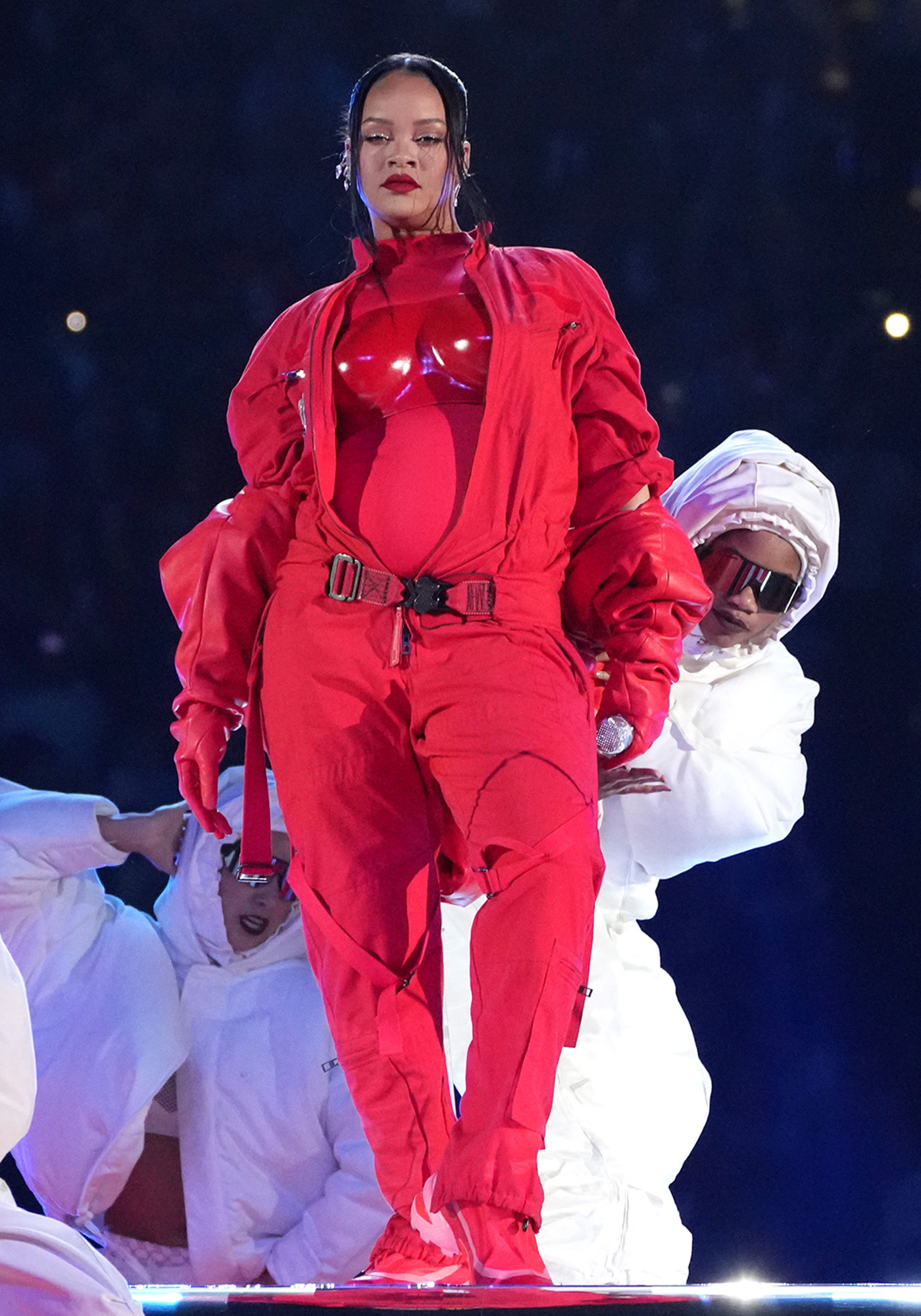 Rihanna występuje na Super Bowl w czerwonym stroju, otoczona tancerzami w białych kostiumach.