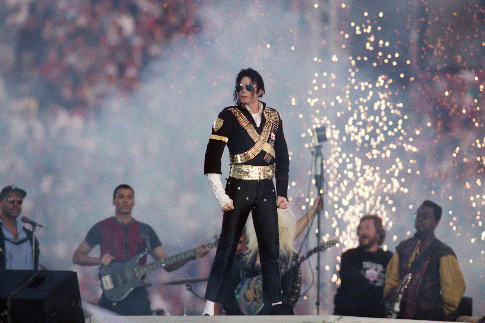 Michael Jackson występuje podczas Super Bowl, otoczony przez zespół i efekty pirotechniczne.